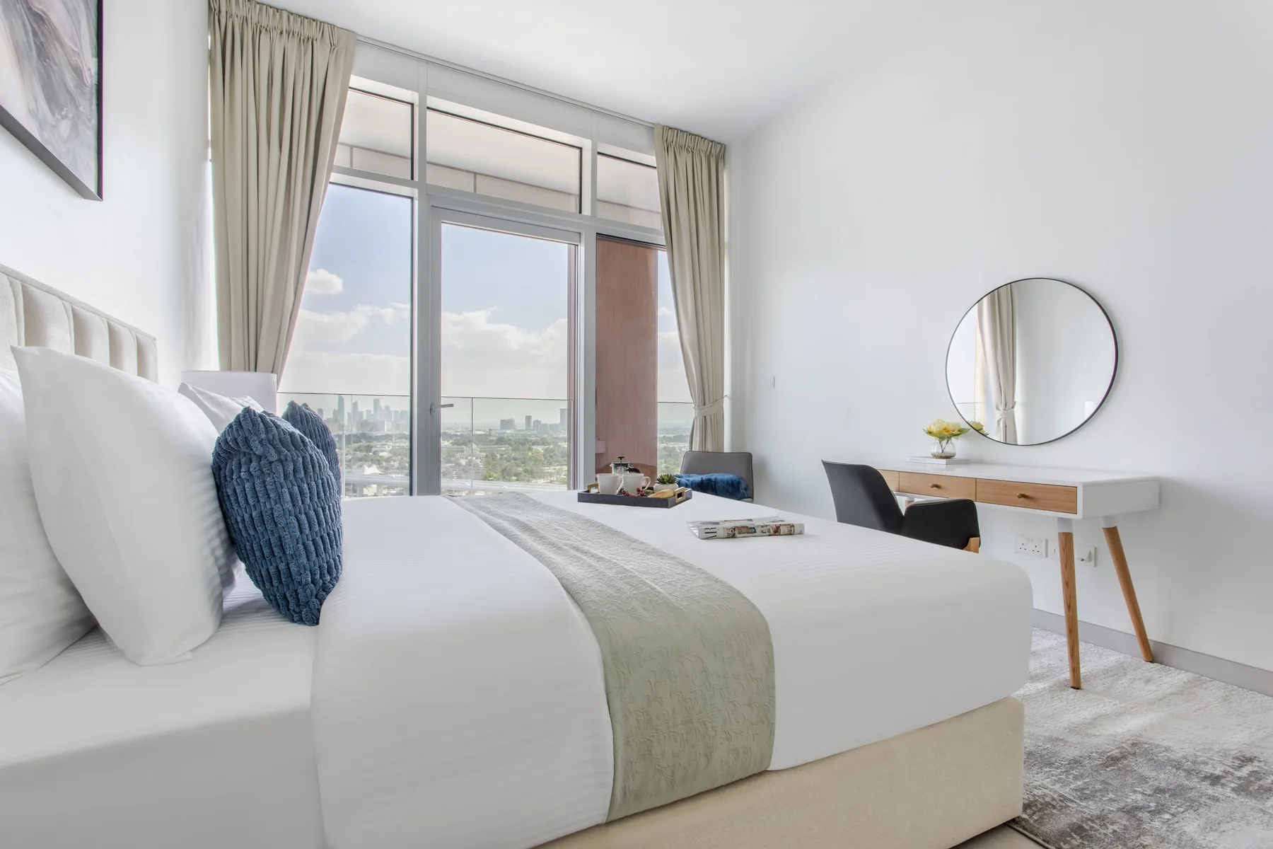 Un dormitorio luminoso con una cama tendida, grandes ventanas y un escritorio.