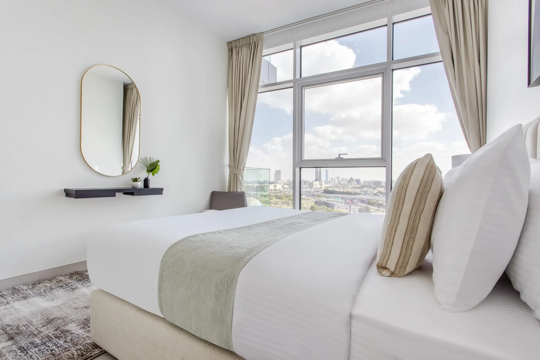Un dormitorio luminoso con una cama bien tendida junto a una gran ventana con vistas a la ciudad.