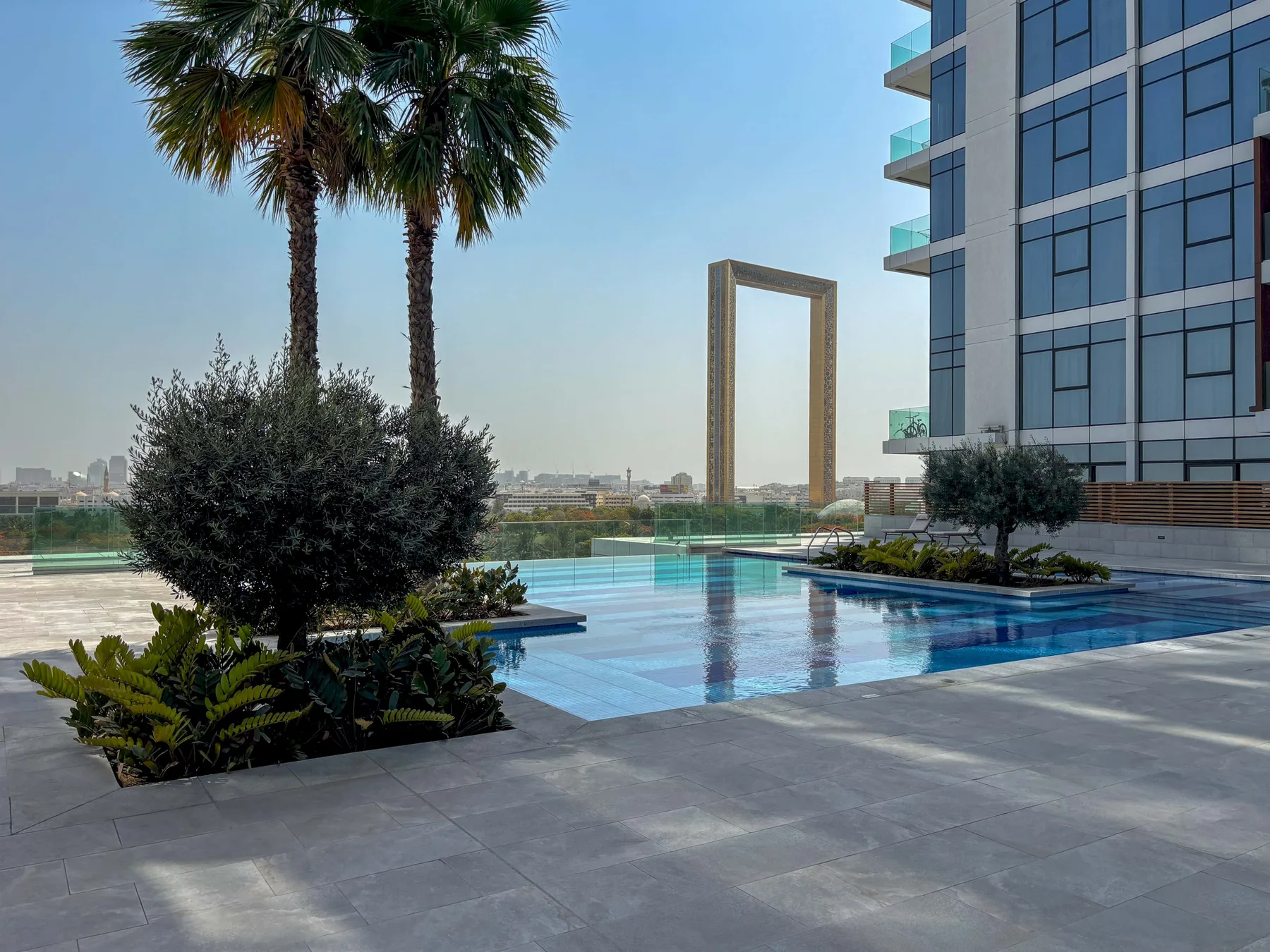 Una piscina exterior ajardinada junto a un moderno edificio de cristal.