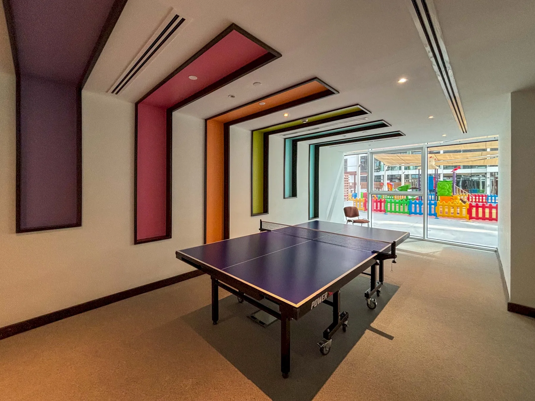 Una sala de recreación con una mesa de ping-pong y paneles geométricos de colores.