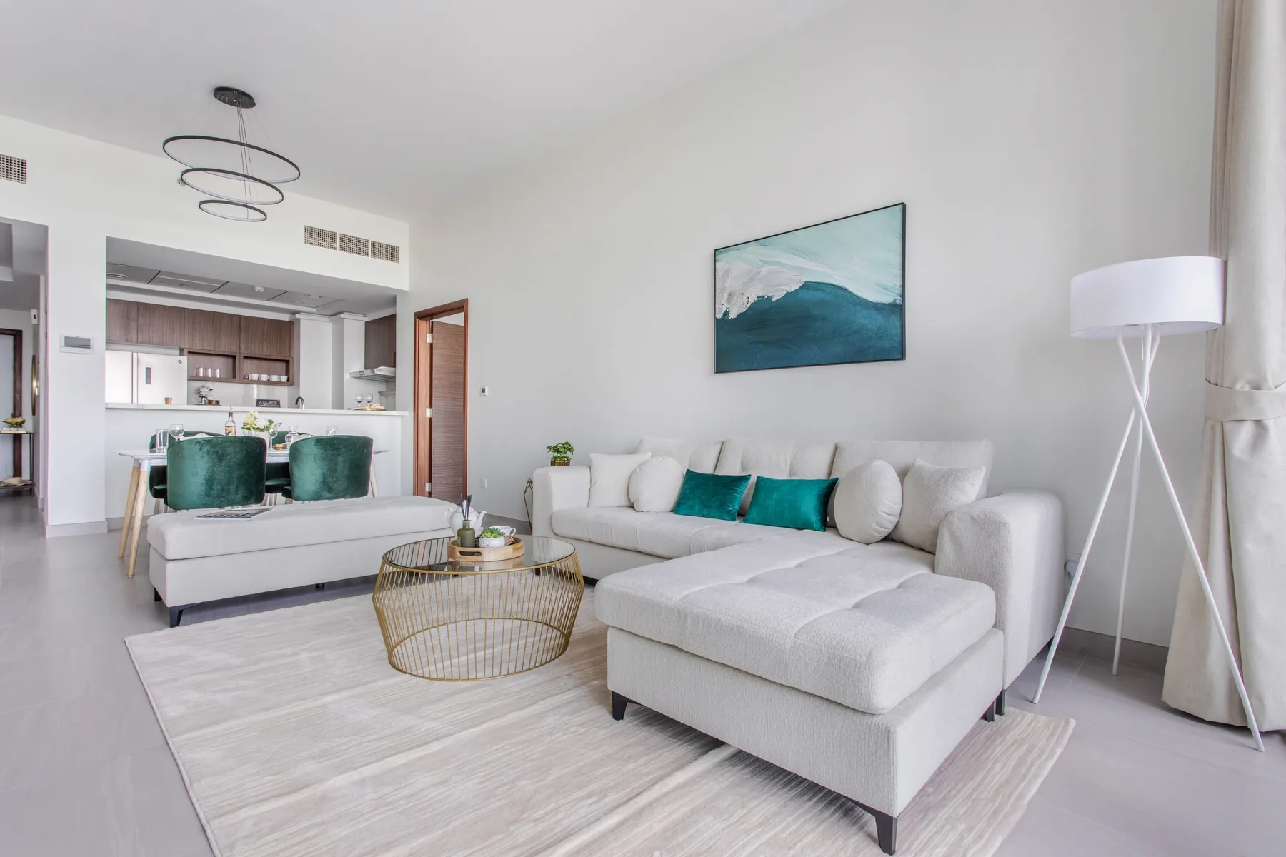 A bright living room with a sectional sofa and an open kitchen behind it.