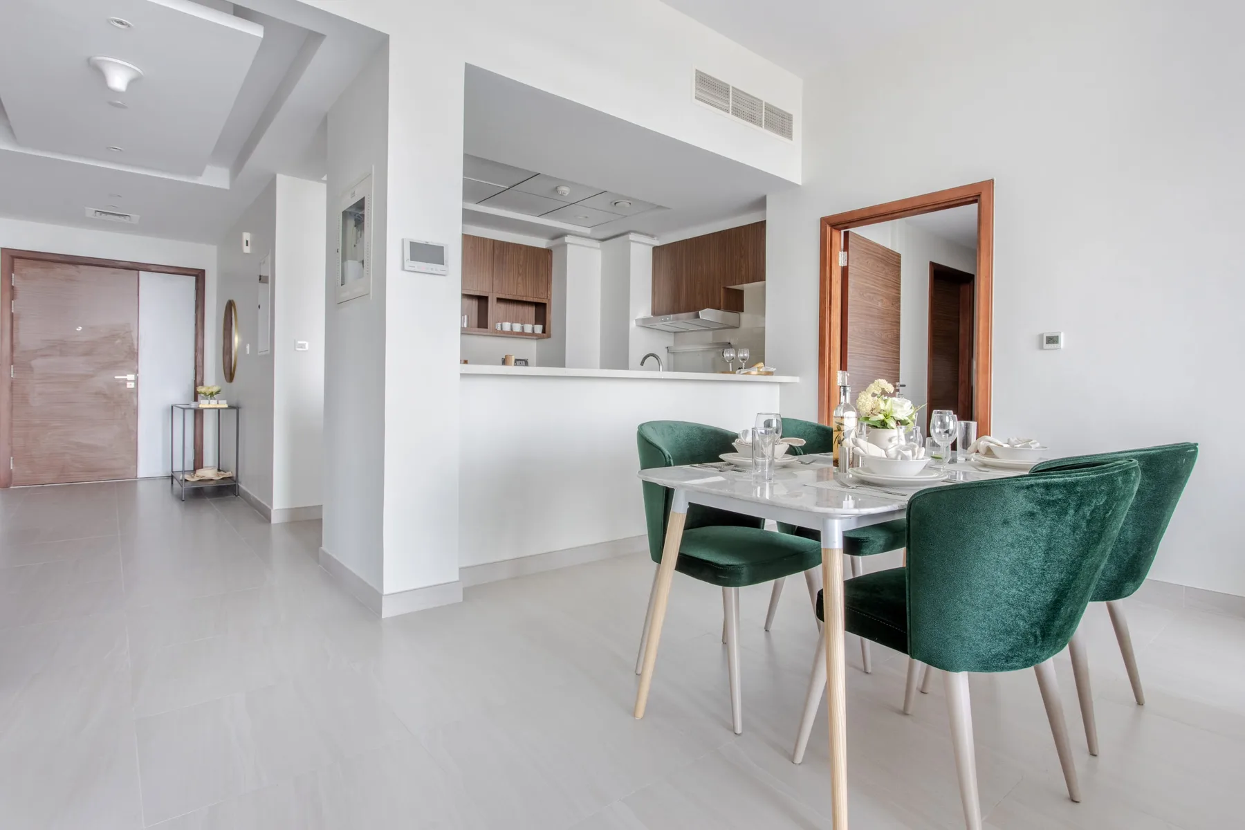 Un comedor luminoso con asientos verdes junto a una cocina abierta.