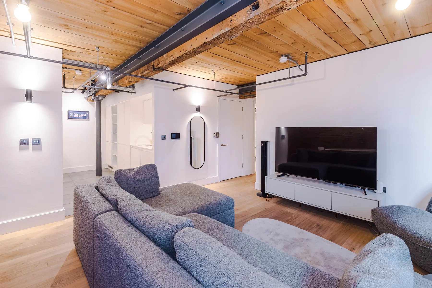 A living room with gray seating and a television beneath a wooden ceiling.