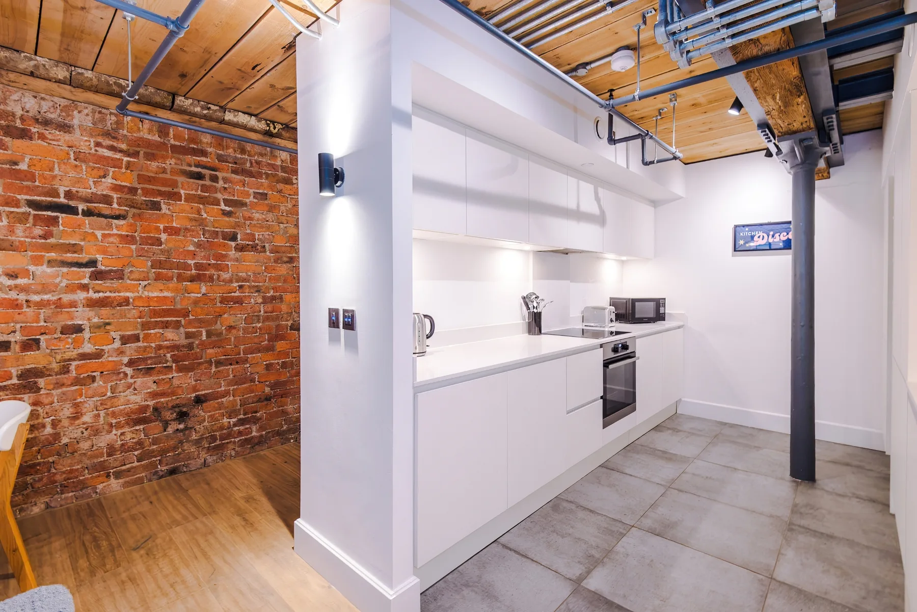 A compact kitchen with white cabinets and exposed brick walls.