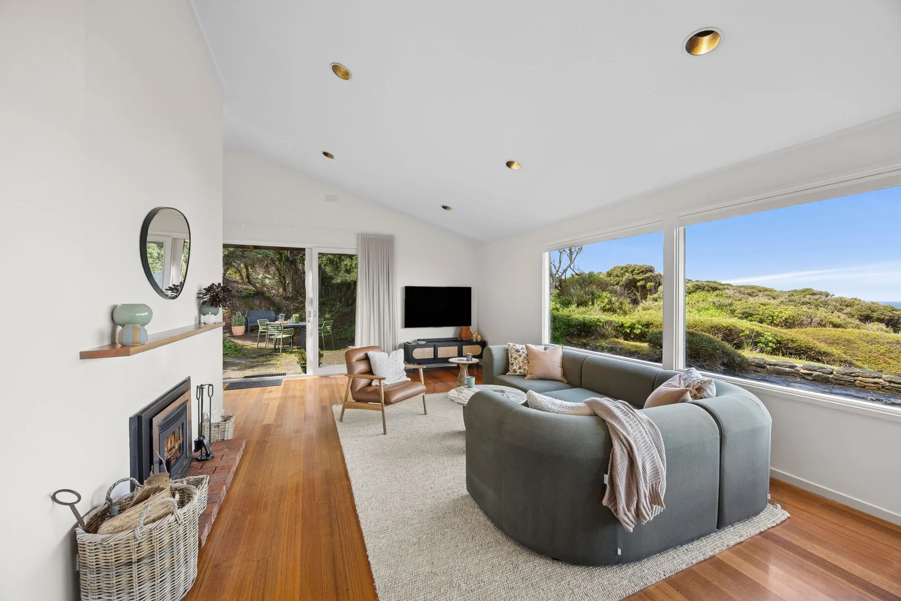 A bright living room with curved seating and large windows overlooking greenery.