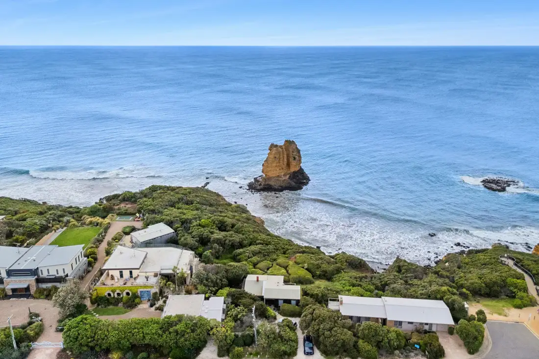 A coastal landscape with blue ocean, rocky shoreline, and buildings among greenery.