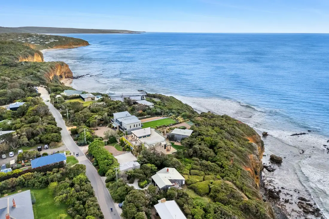 Aerial view of coastal homes beside a winding road and rocky shoreline.