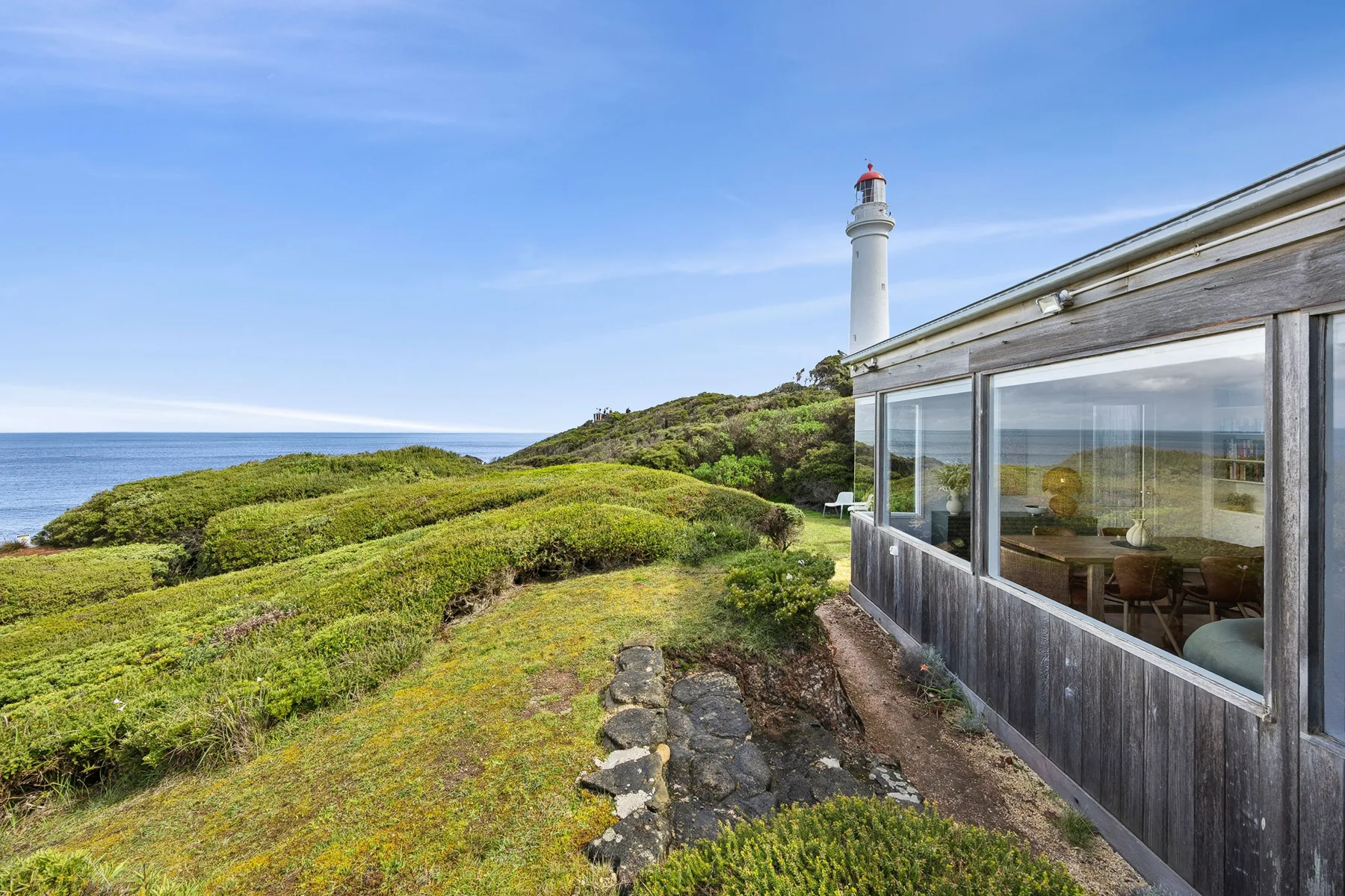 A glass-walled building overlooks green coastal hills and the ocean.