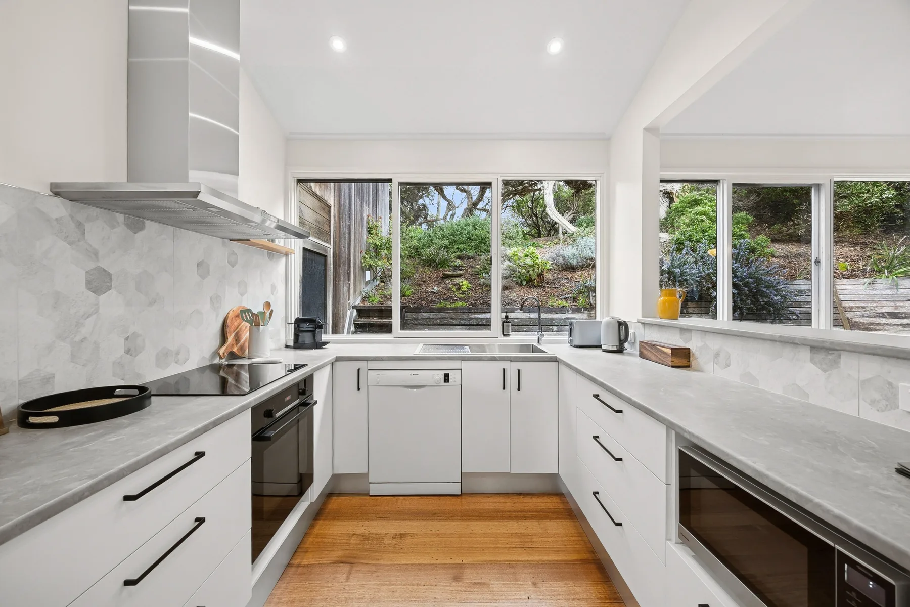 A bright kitchen with white cabinetry, pale countertops, and wide windows.