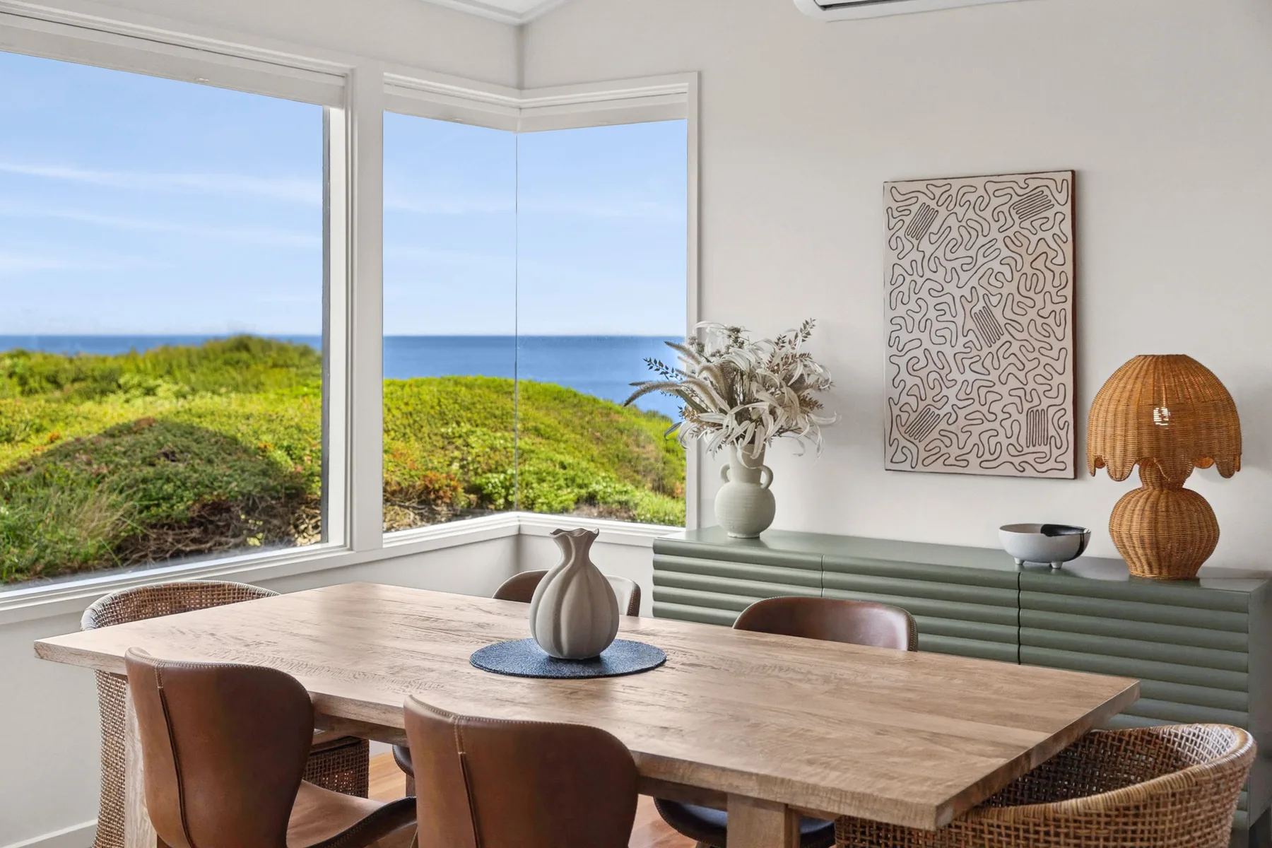 A dining area with a wooden table beside large windows overlooking the ocean.