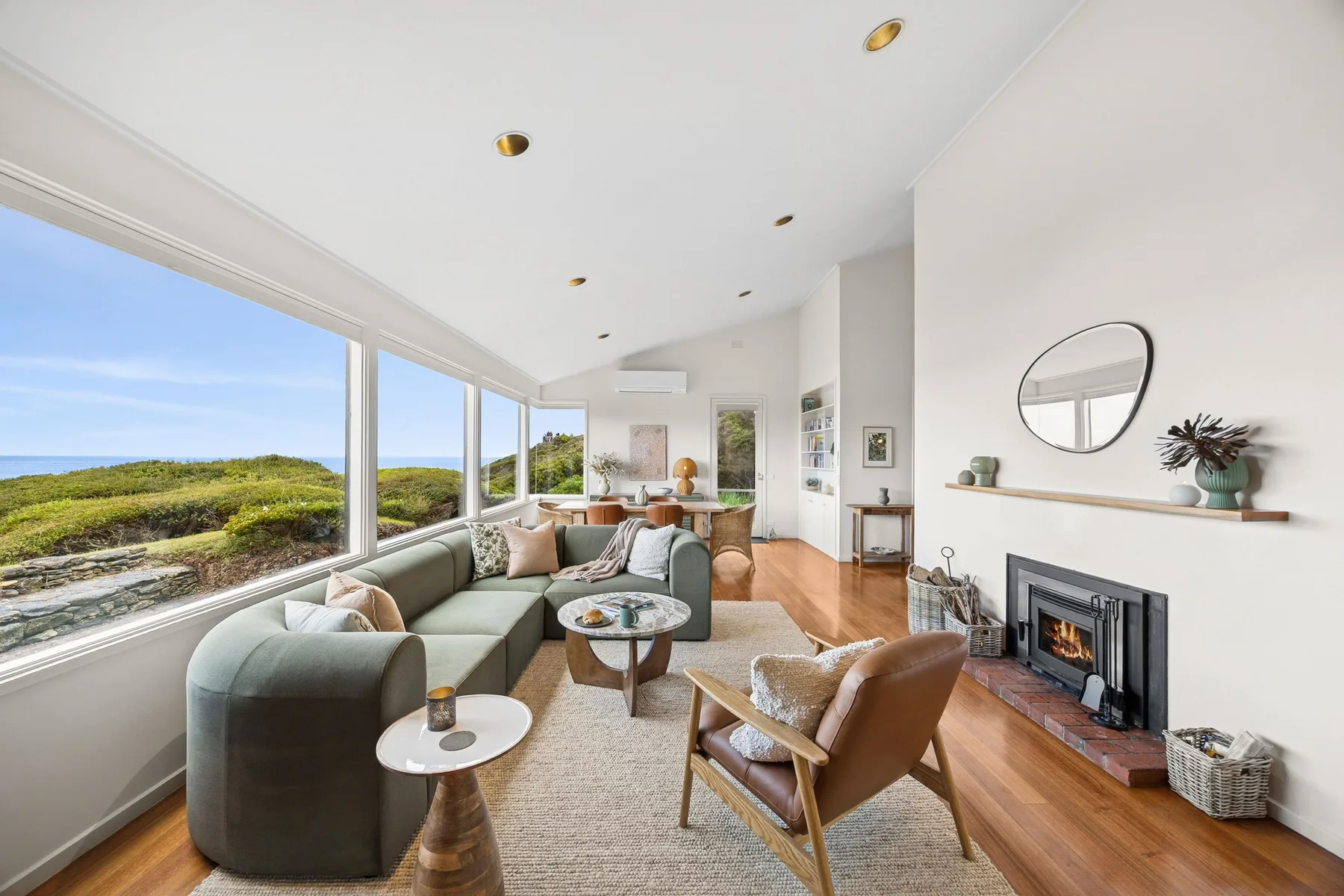 A bright living room with broad windows overlooking a green coastal landscape.