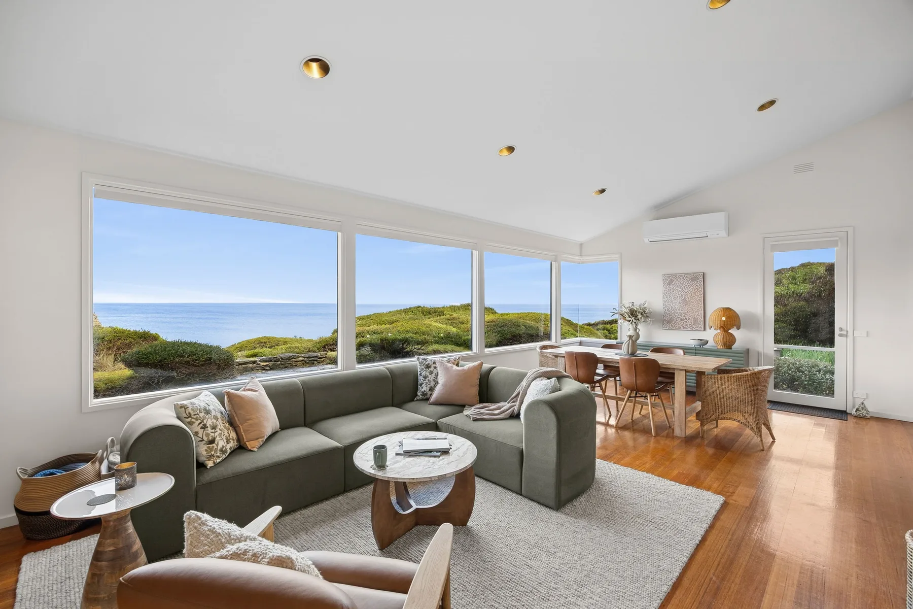 A bright living and dining area opens onto coastal views through large windows.