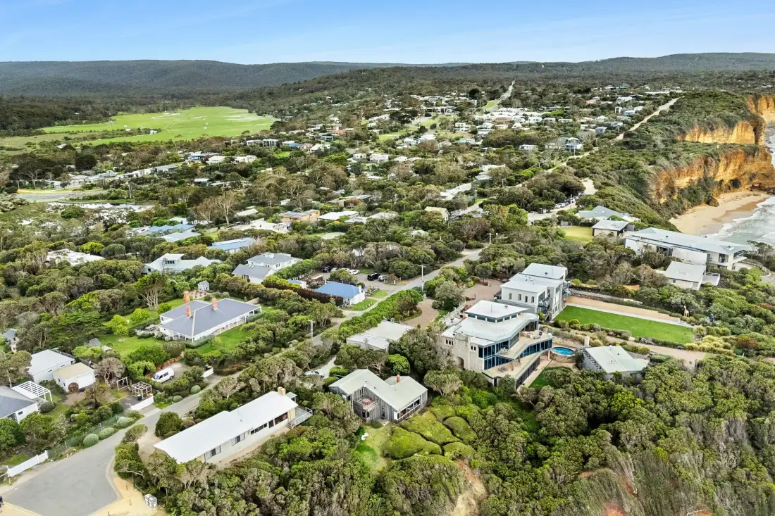 An aerial view of homes among greenery beside coastal cliffs.