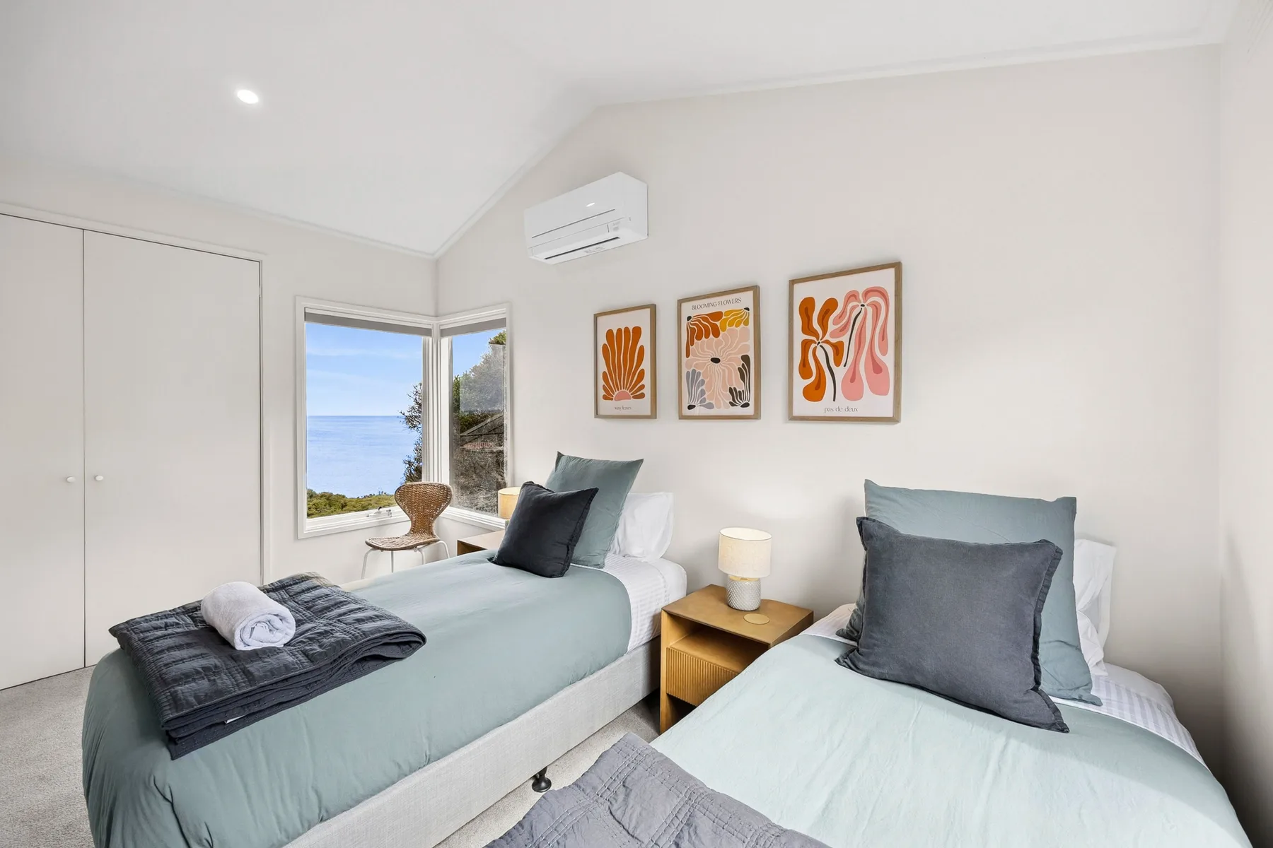 A bright bedroom with two beds, colorful wall art, and a window overlooking the water.