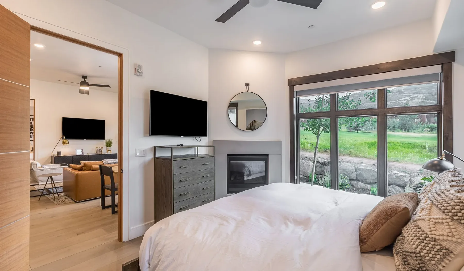 Un dormitorio con cama, chimenea y grandes ventanas con vistas a la vegetación.