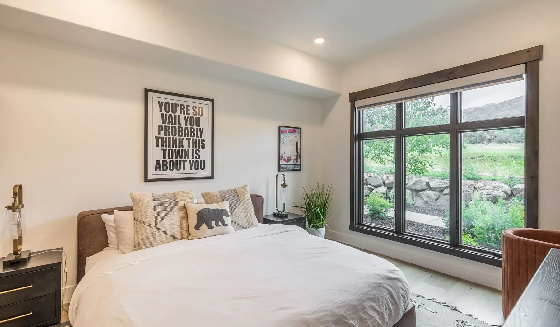 Un dormitorio con una cama junto a una gran ventana con vistas a la vegetación.