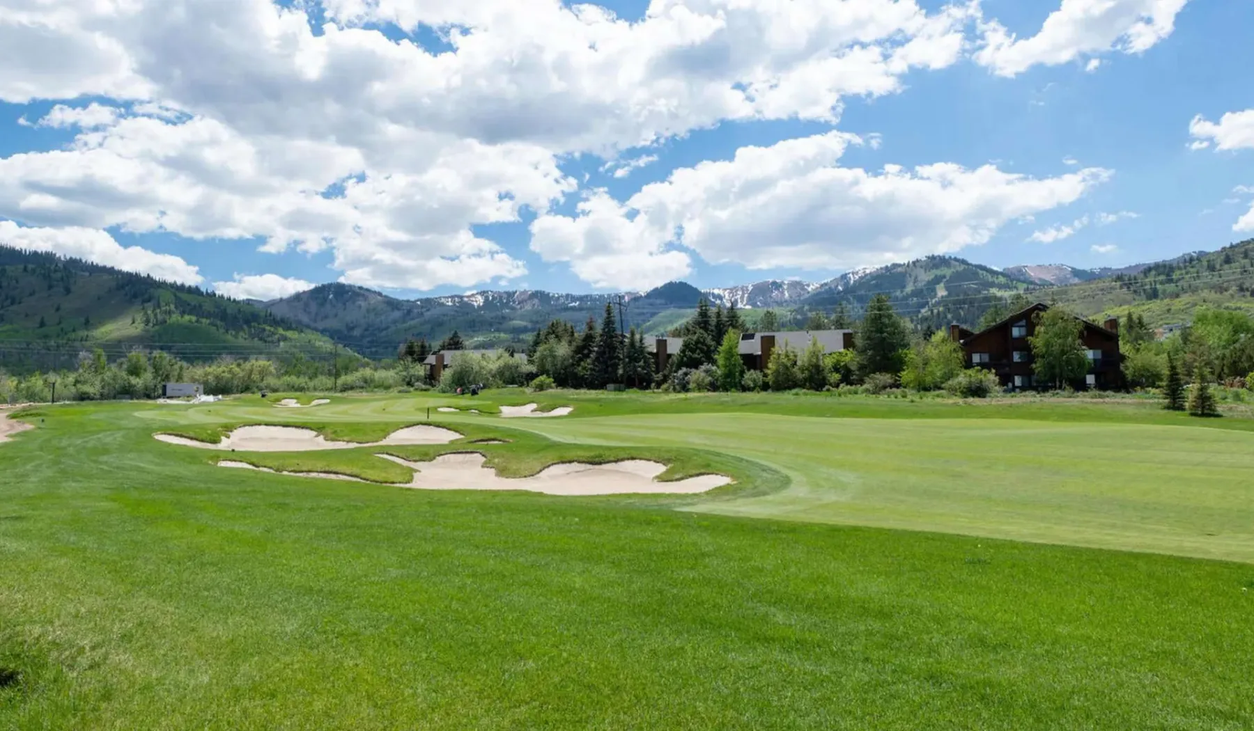 Un campo de golf con trampas de arena se extiende por un valle verde bajo las montañas.