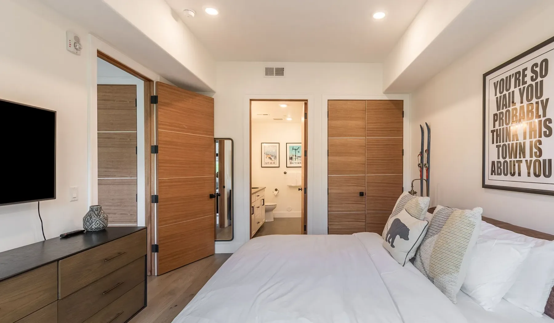 Un dormitorio con una cama, puertas de acabado de madera y un televisor en la pared.