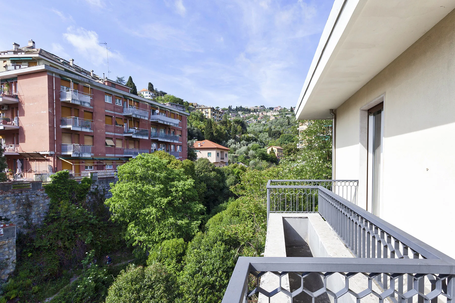 Un balcón da a colinas frondosas y edificios de apartamentos cercanos.