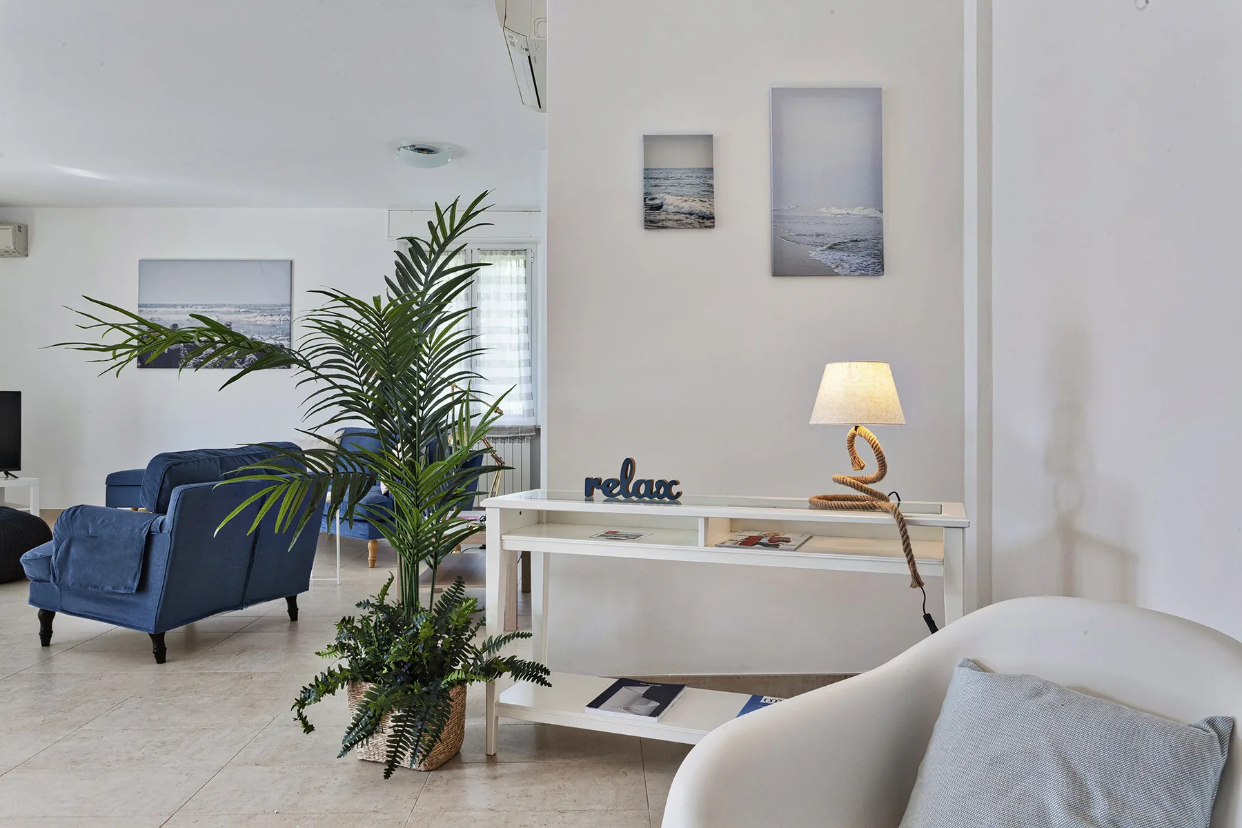 Una sala luminosa con asientos azules, una palmera en maceta y una consola.