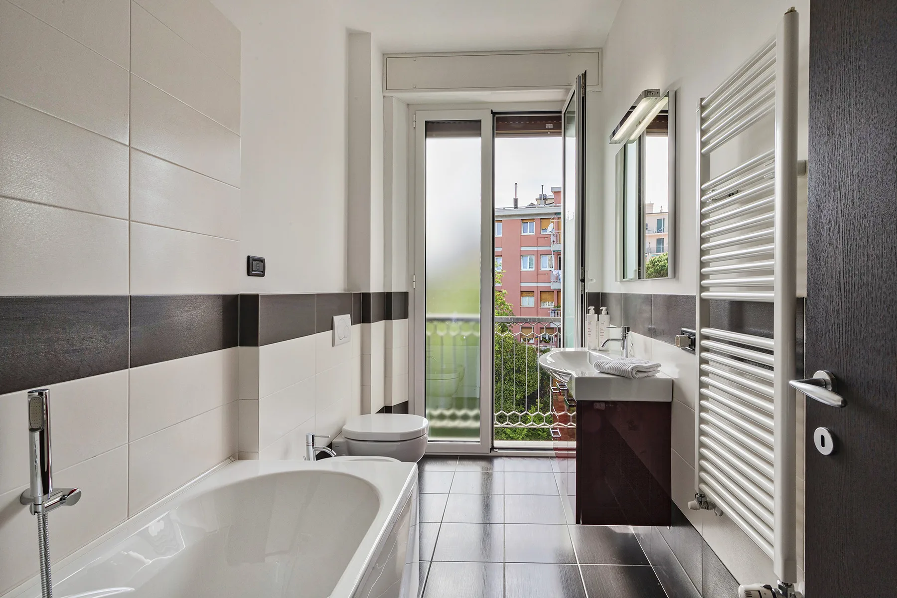 Un baño alicatado con bañera, lavabo y puertas de vidrio que dan a un balcón.