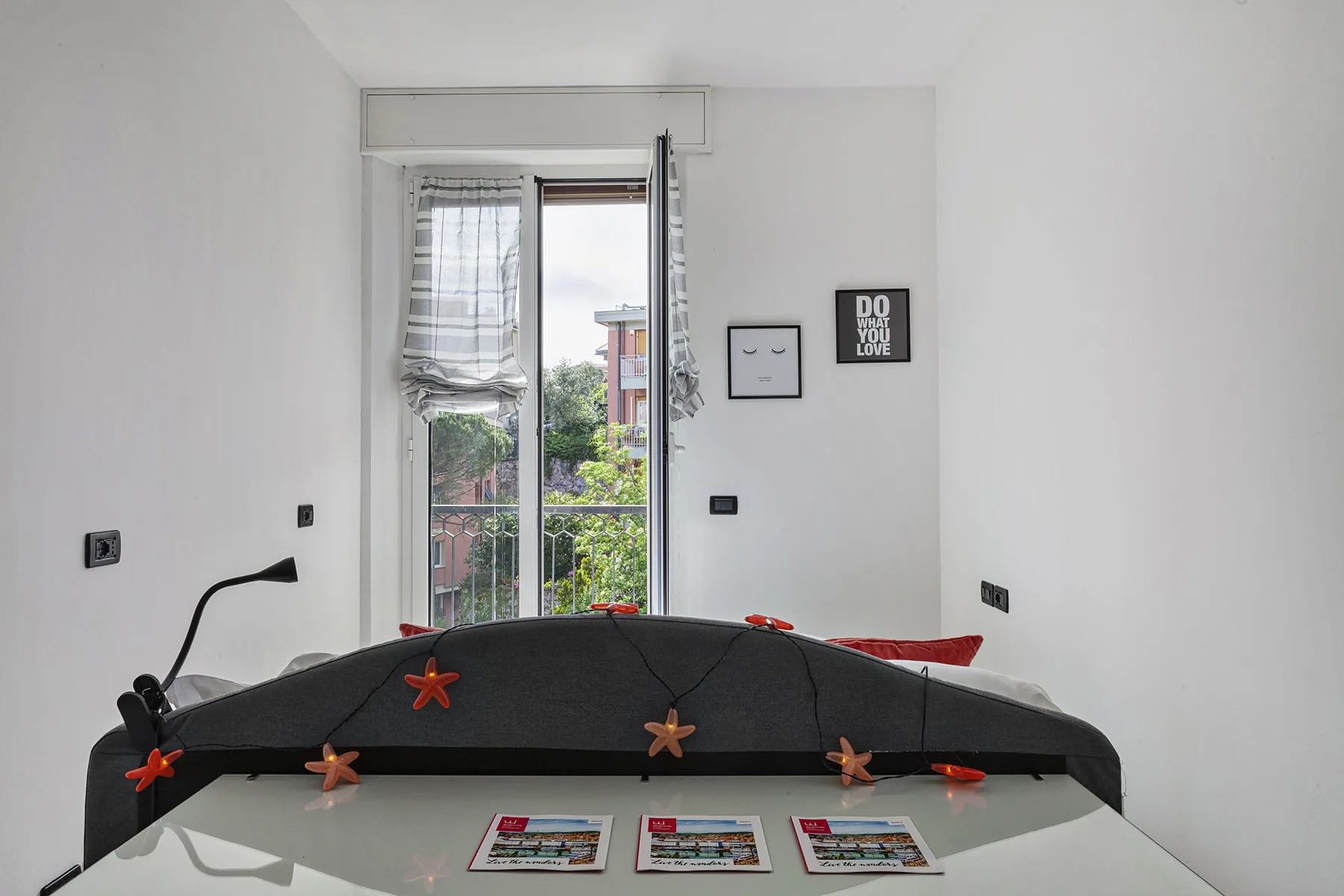 Un dormitorio con una cama oscura bajo una ventana abierta.