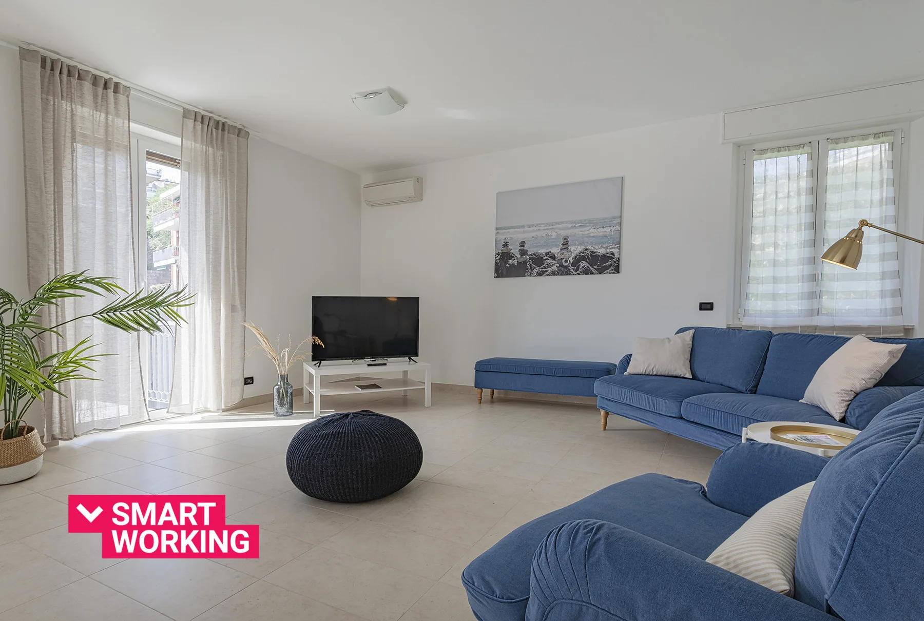 Una sala luminosa con asientos azules, un televisor y ventanales.
