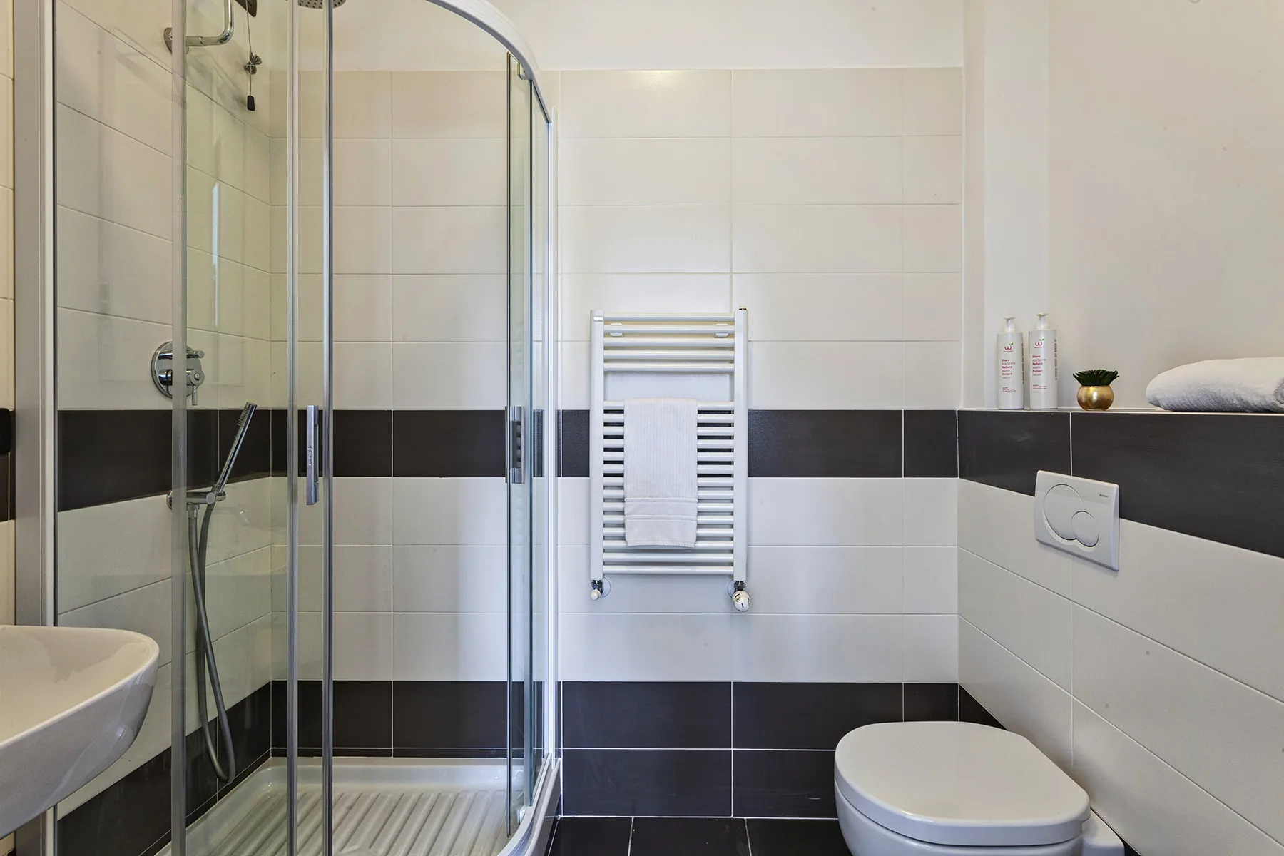 Un baño con azulejos, ducha de vidrio, toallero calefactable y váter.