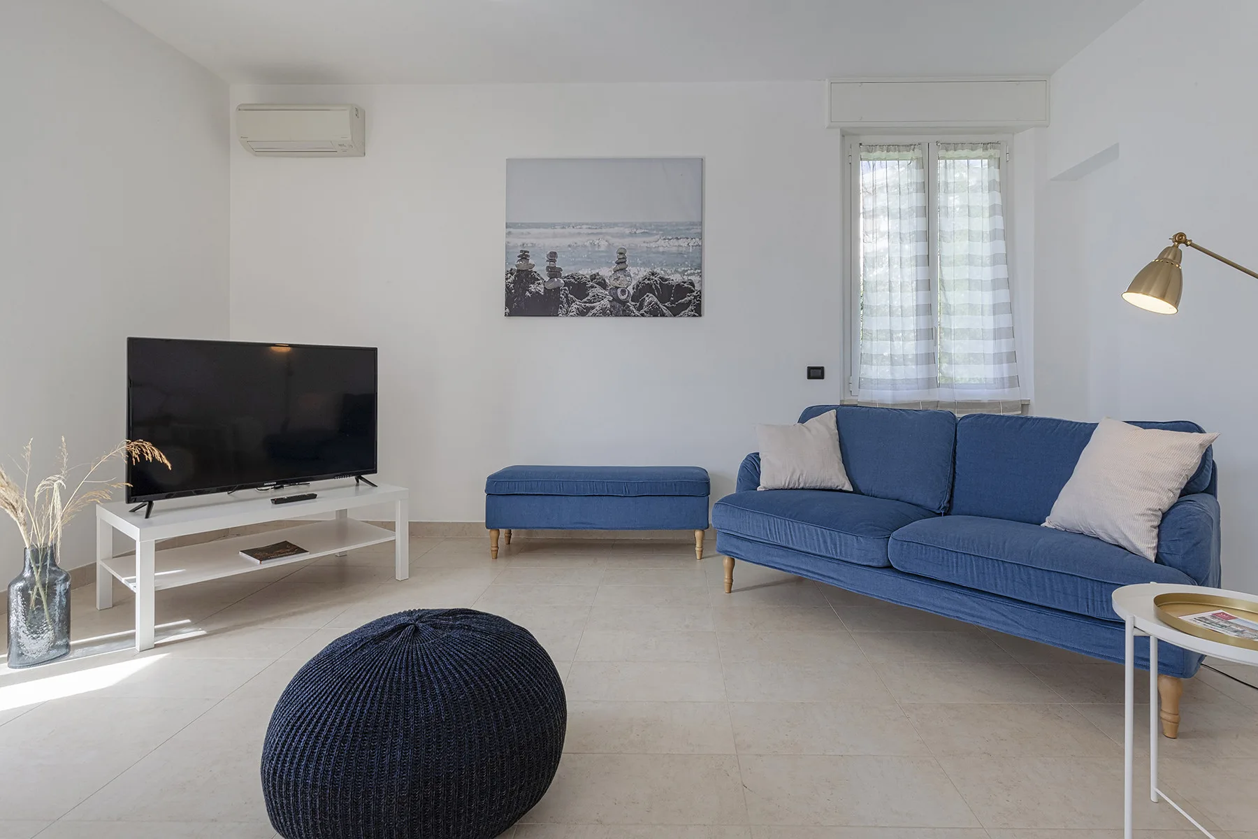 Una sala luminosa con asientos azules, un televisor y una ventana con cortinas.