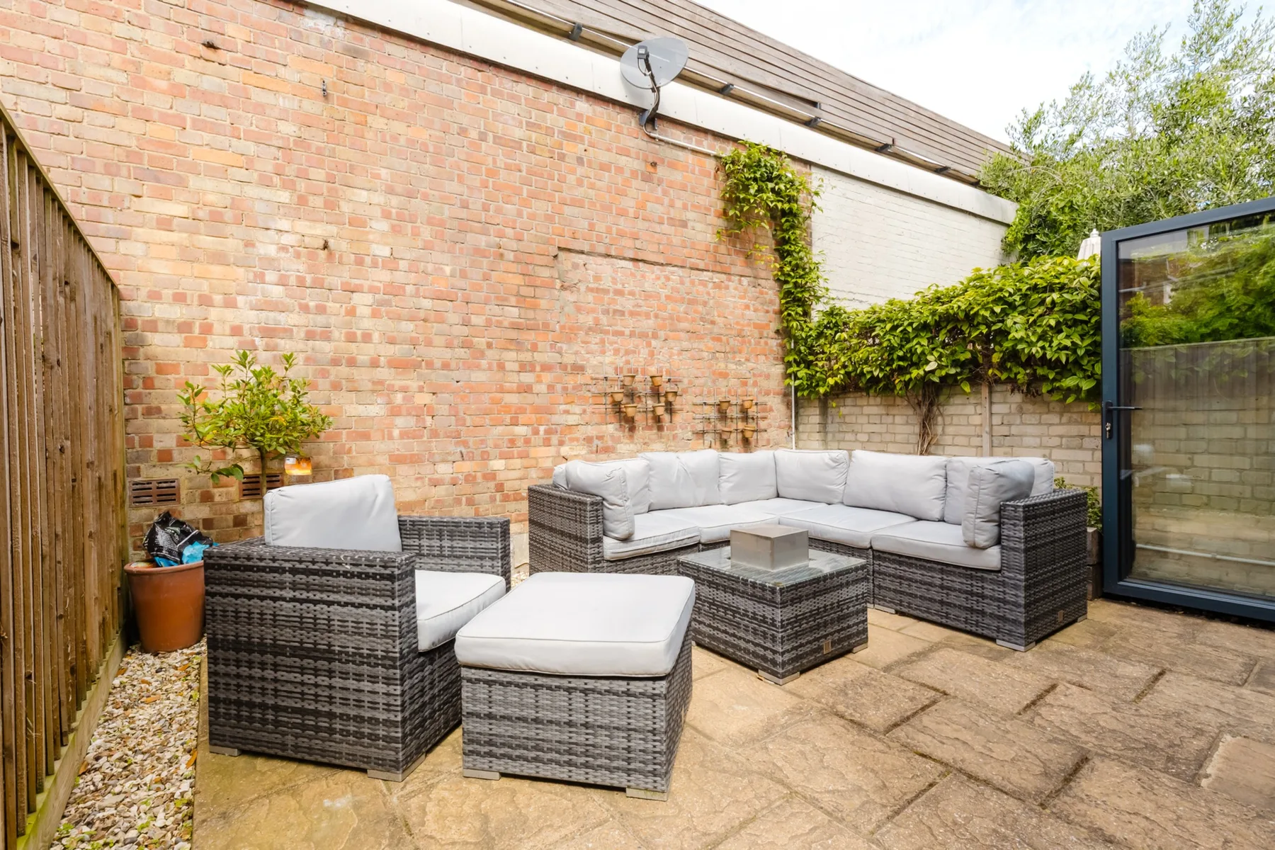 A paved patio features wicker seating and a brick wall.