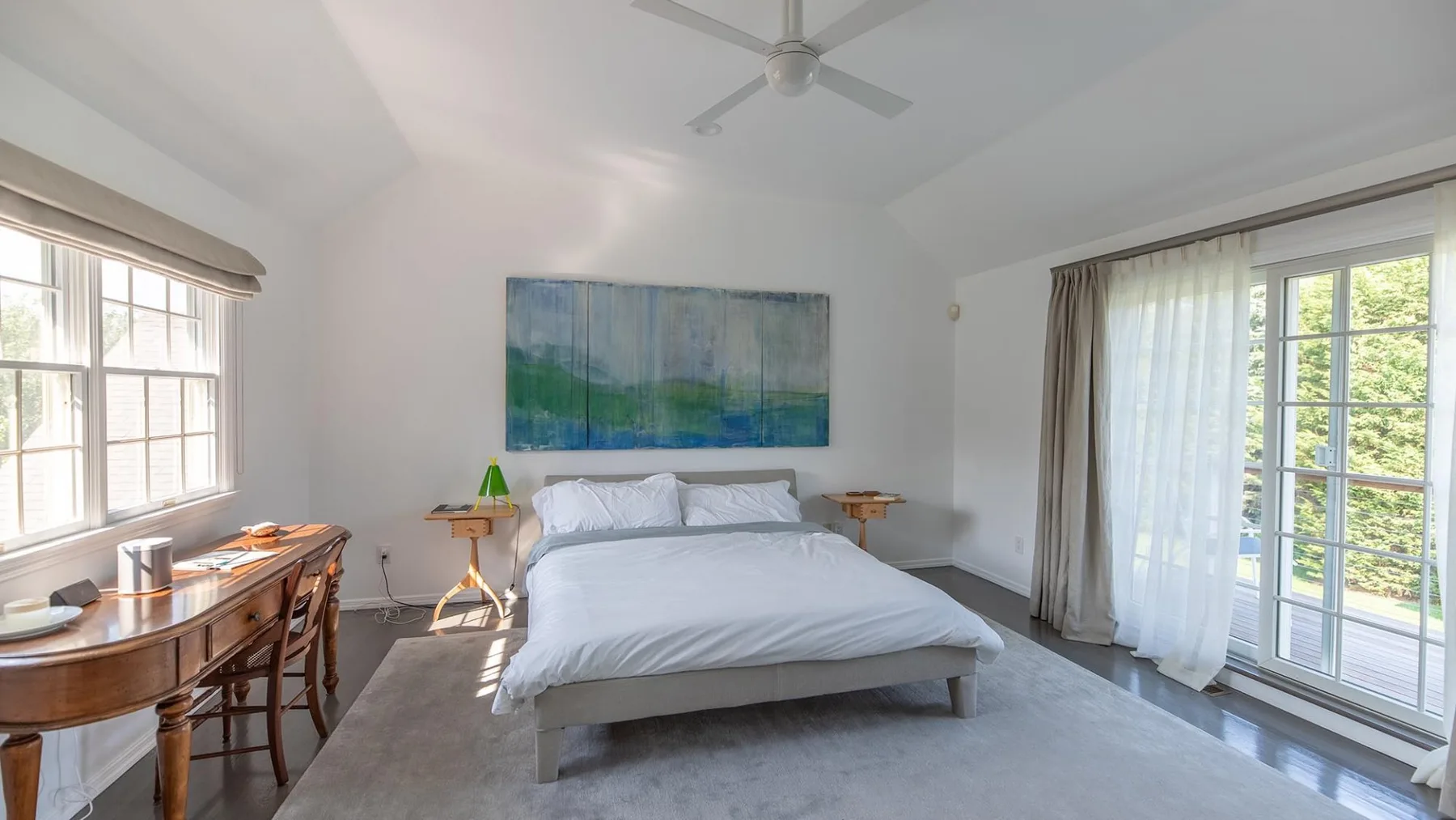 Un dormitorio luminoso con una cama tendida y grandes ventanas.