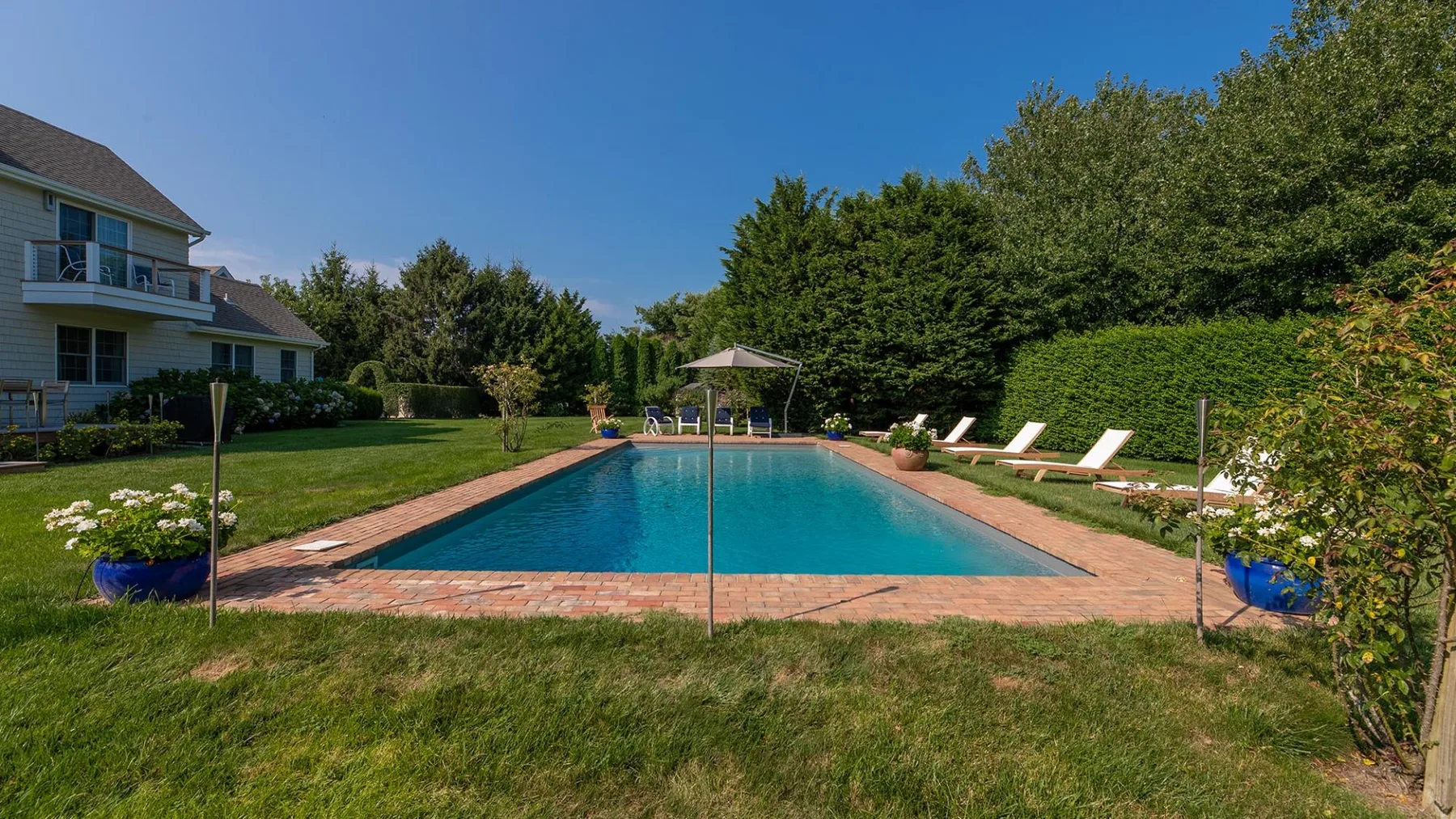 Una piscina al aire libre está junto a un césped y un jardín ajardinado.
