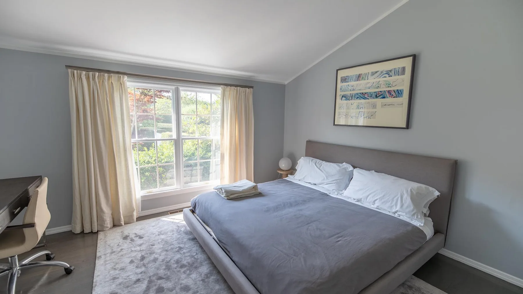 Un dormitorio con una cama grande y una ventana luminosa enmarcada por cortinas.