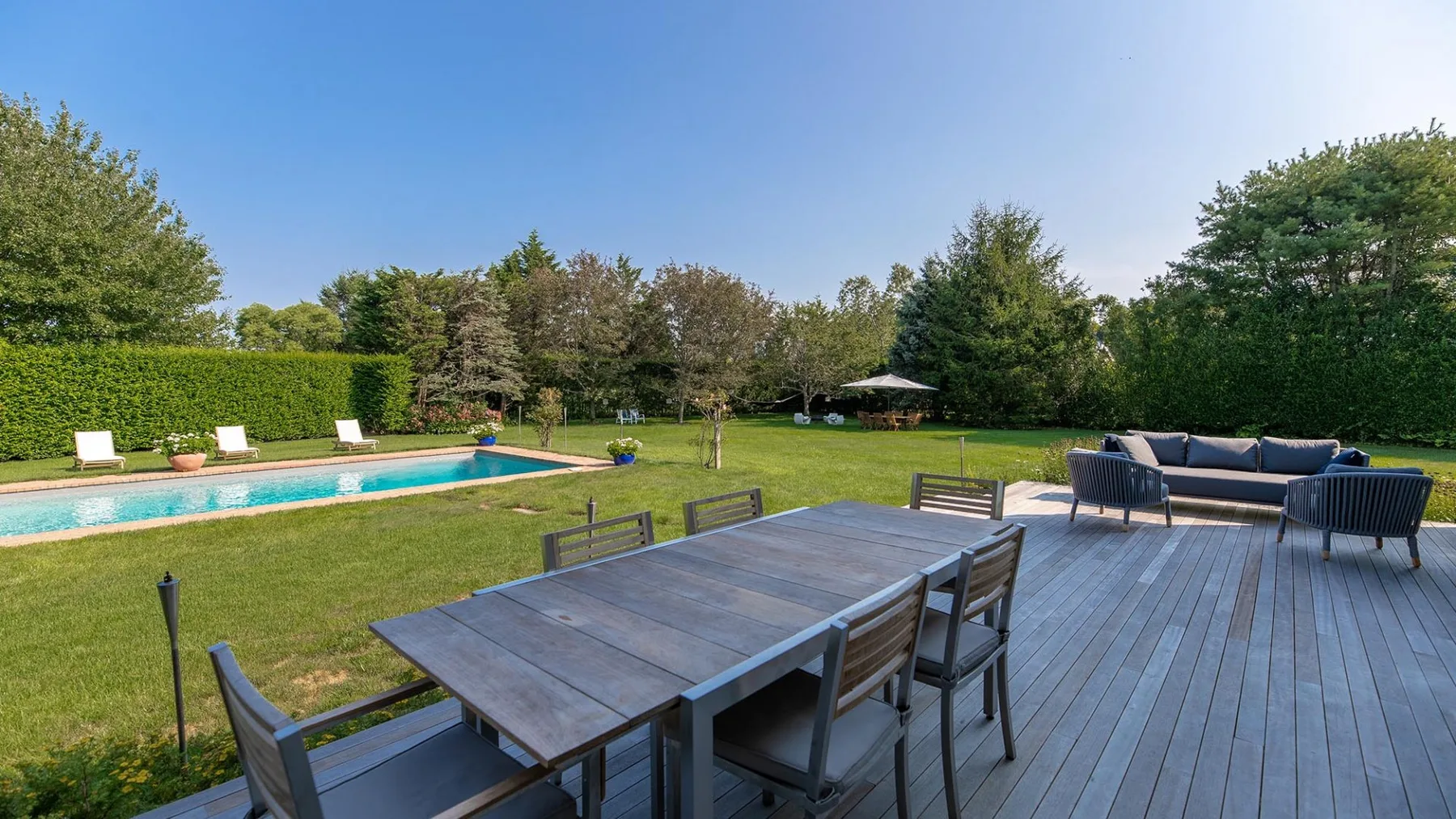 Una zona de comedor al aire libre da a una piscina y un amplio césped verde.