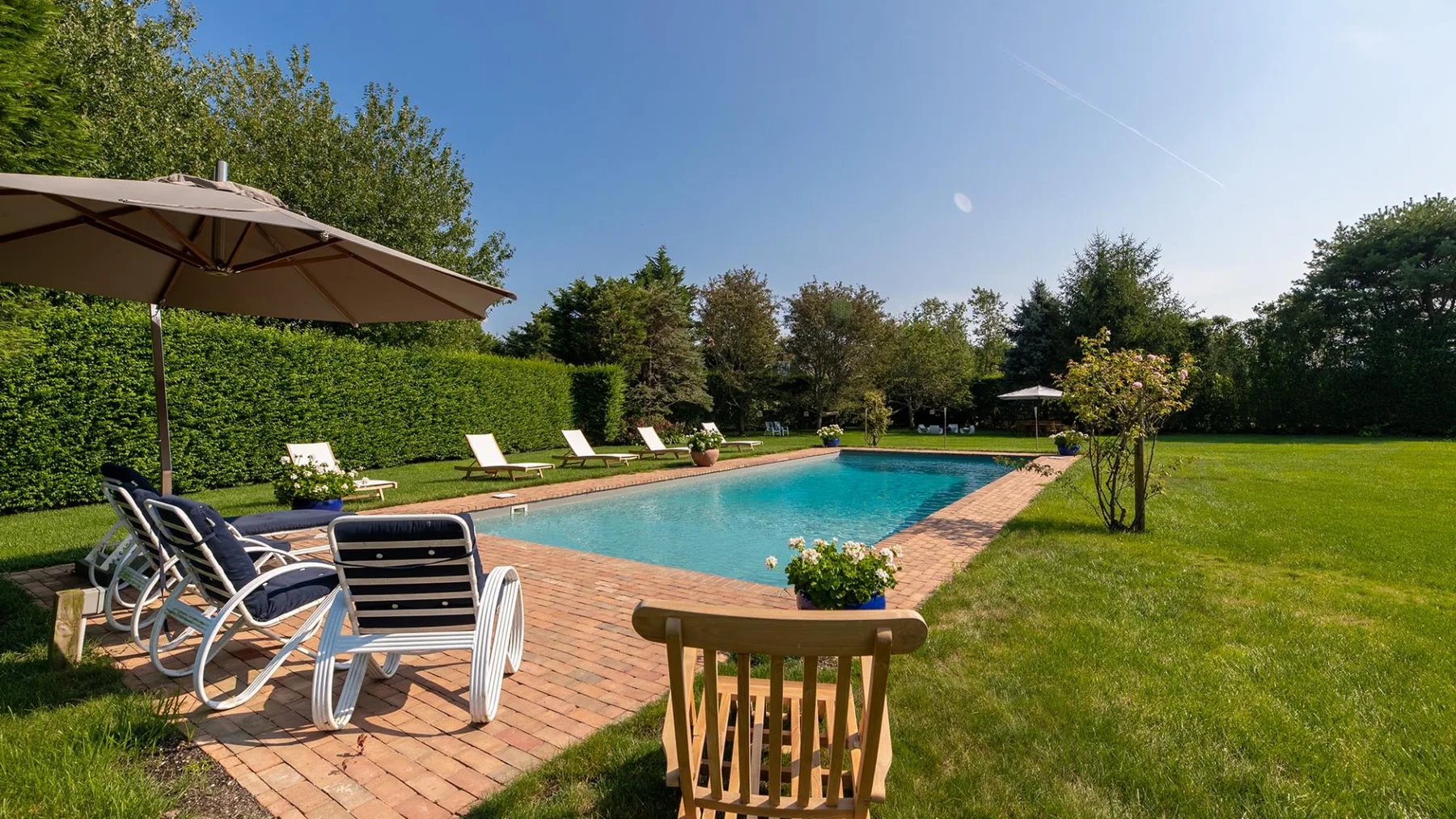 Una piscina al aire libre está rodeada por un patio de ladrillo y césped verde.