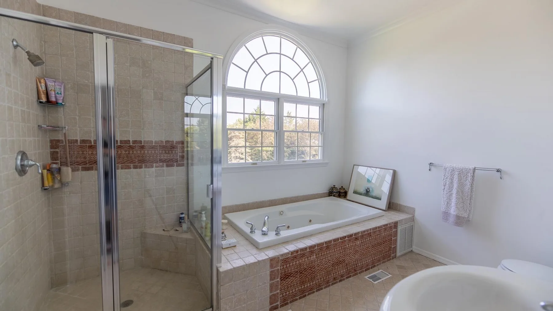 Un baño luminoso con ducha alicatada, bañera y una gran ventana arqueada.