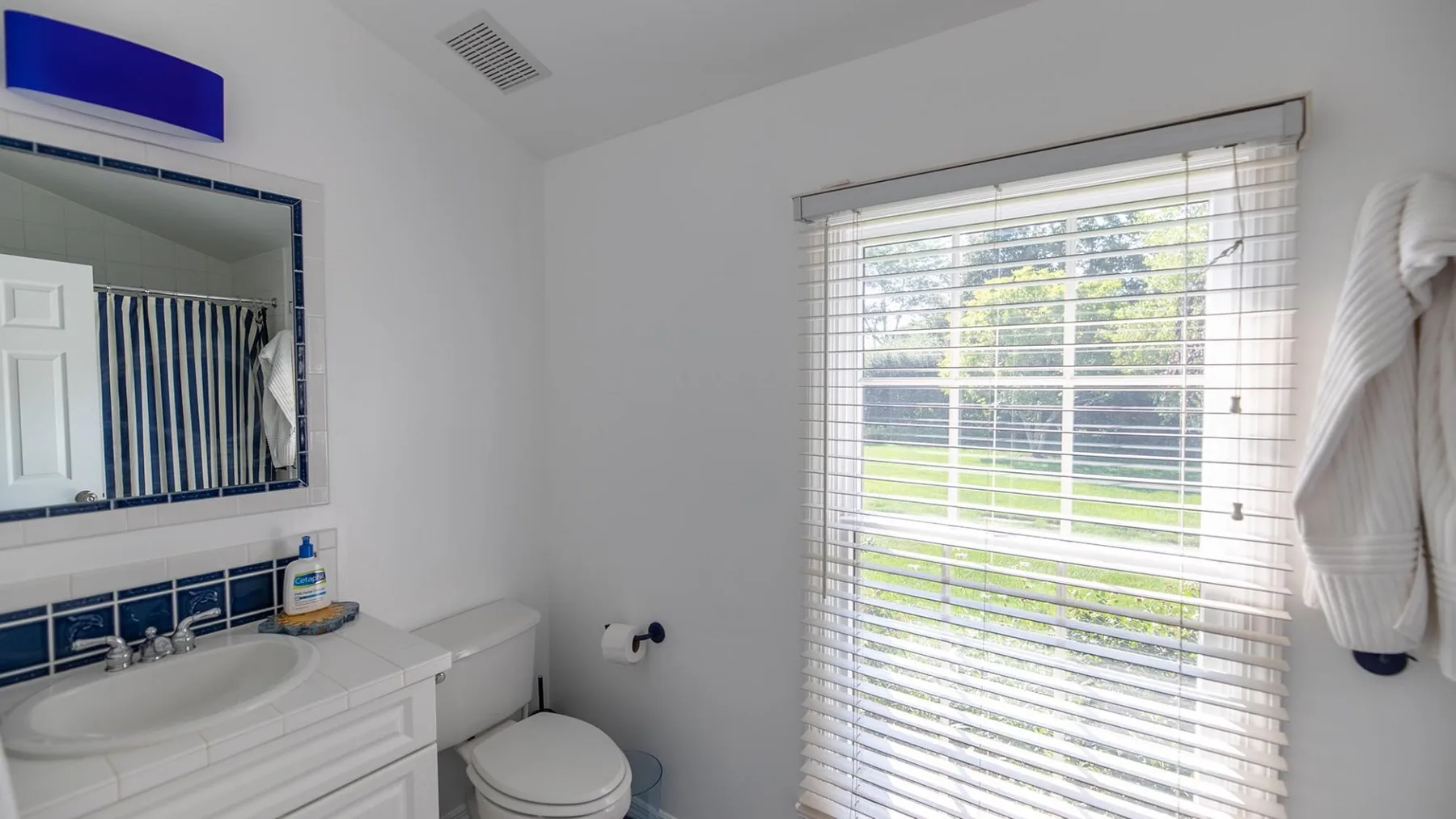 Un baño con lavabo, inodoro y una ventana con persianas.
