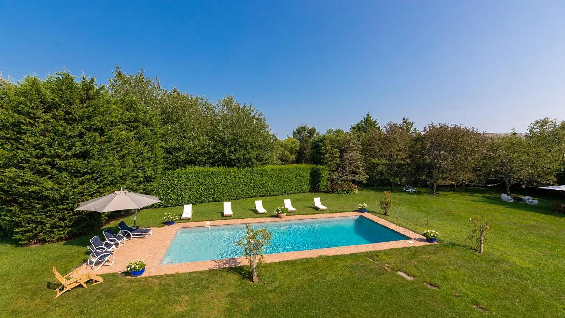 Una piscina está en un jardín con césped, rodeada de árboles.