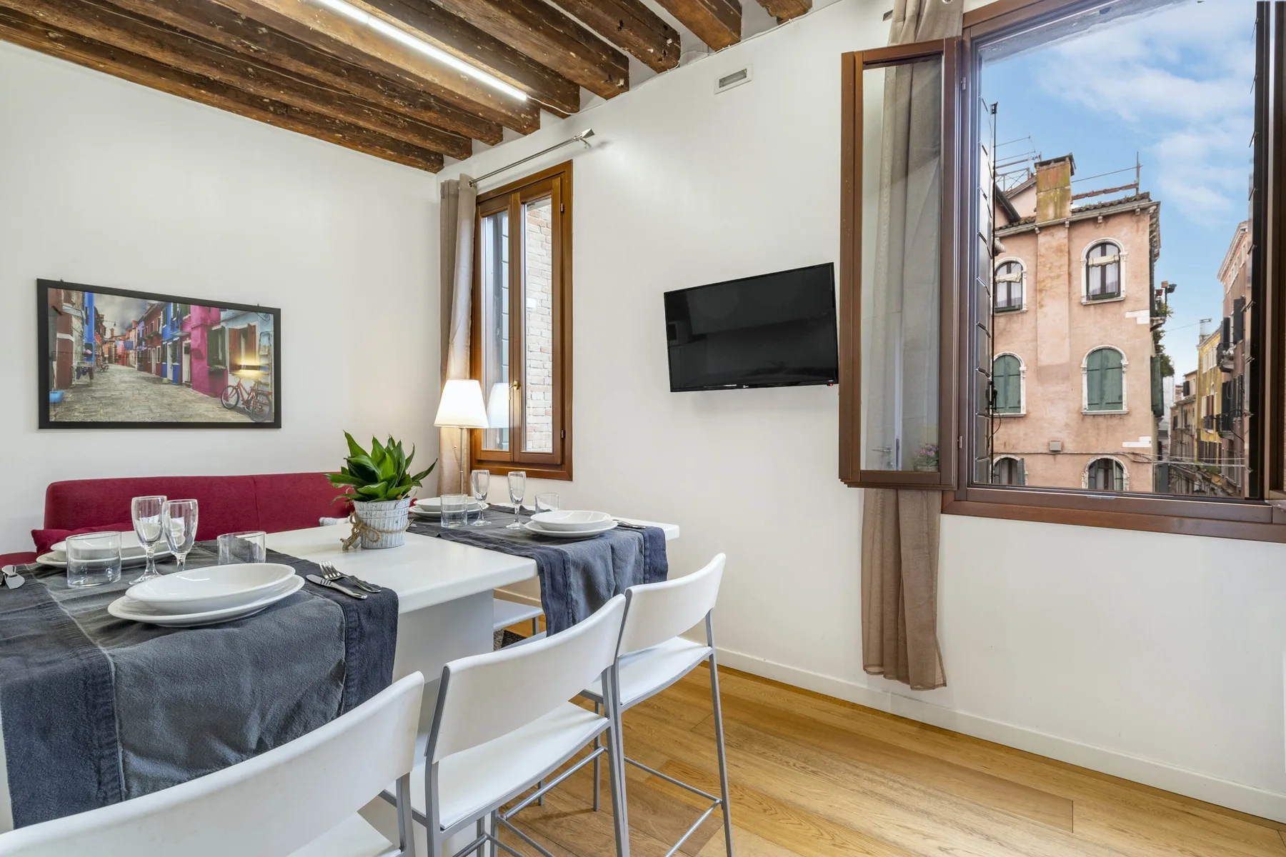 A dining area with a set table beside a large window overlooking nearby buildings.