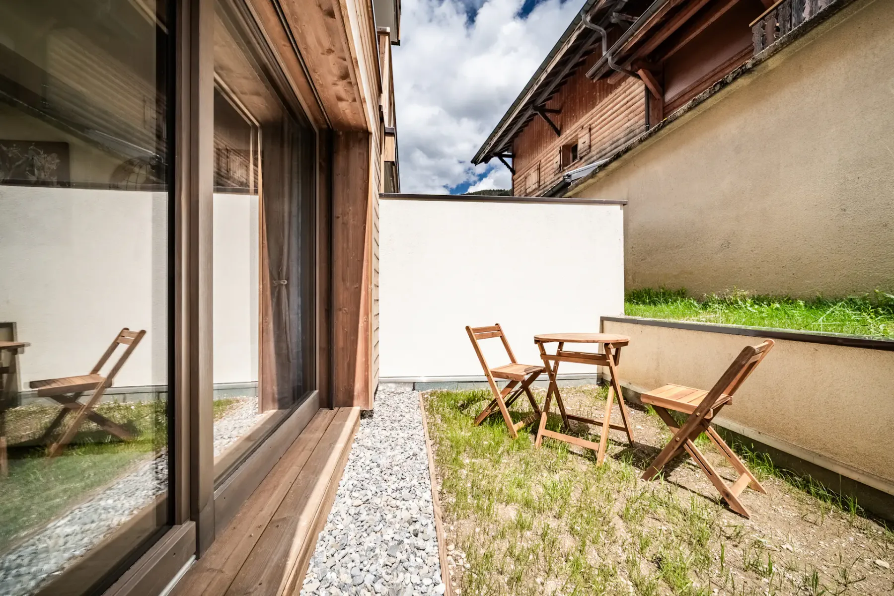 A small outdoor patio with wooden seating, gravel, and a patch of grass.