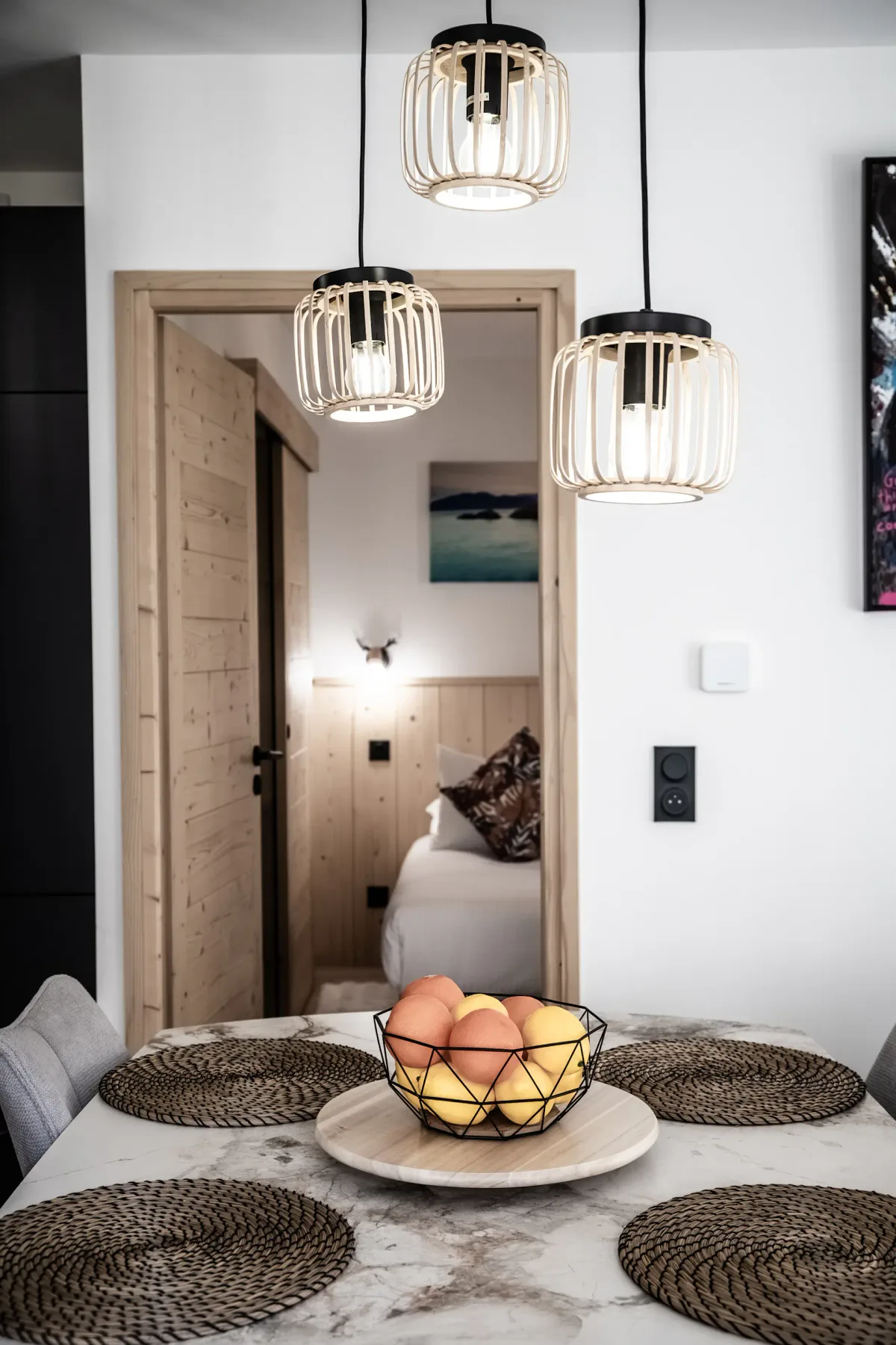 Dining area with a pale stone table, woven placemats, and pendant lights.