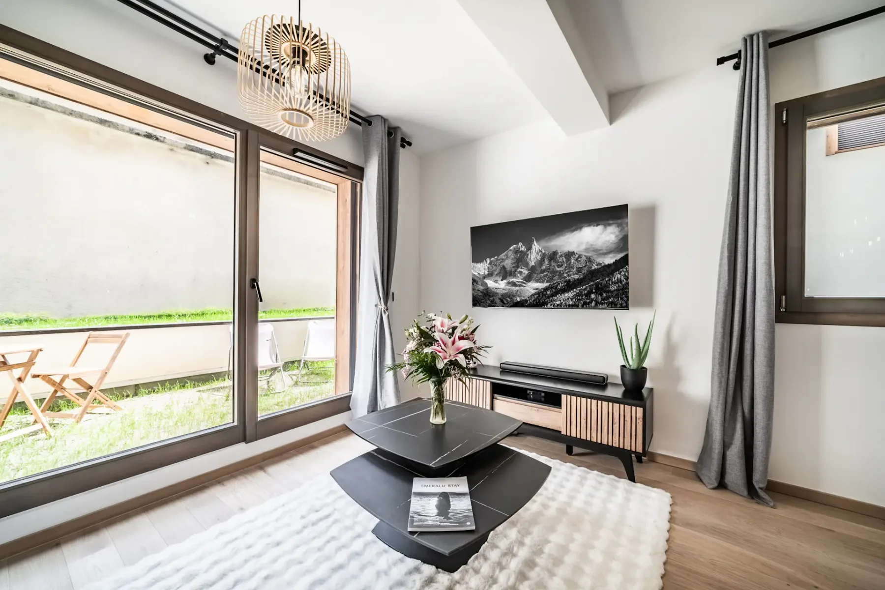 A bright living room with dark seating, a low table, wall art, and large windows.