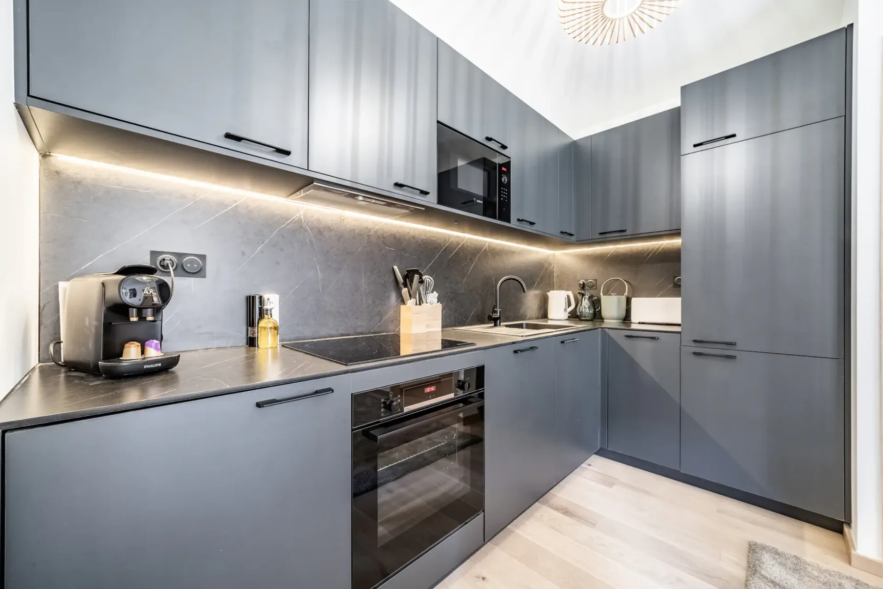 A modern kitchen with gray cabinets, a countertop coffee machine, and built-in appliances.