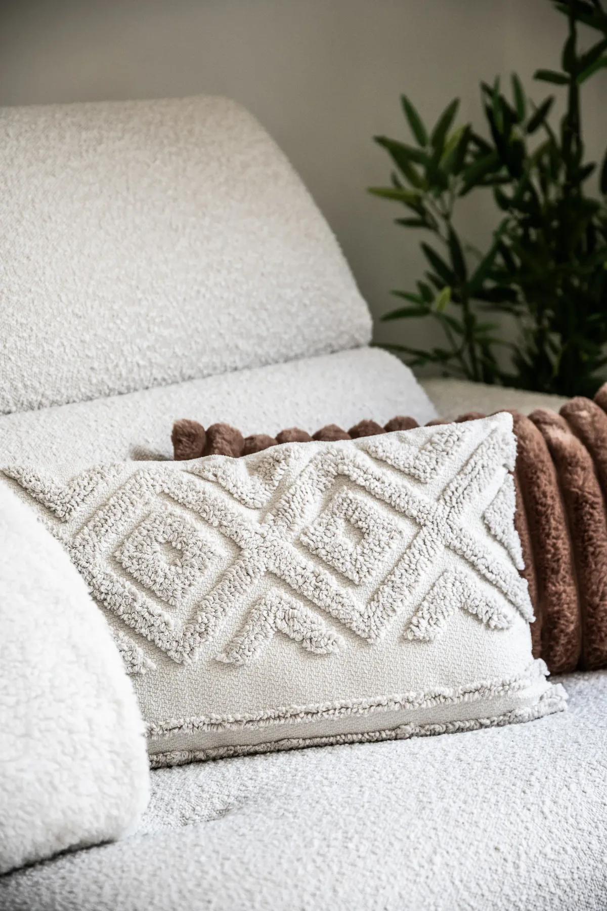 A white textured sofa holds a cream cushion with a raised geometric pattern and a brown throw.