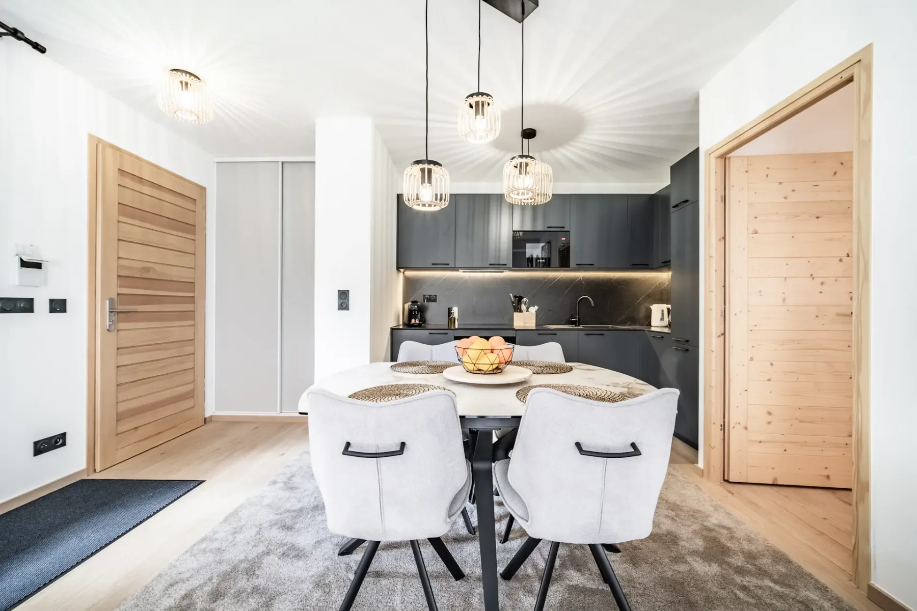 A dining area with a set table, light seating, and a dark kitchen behind it.