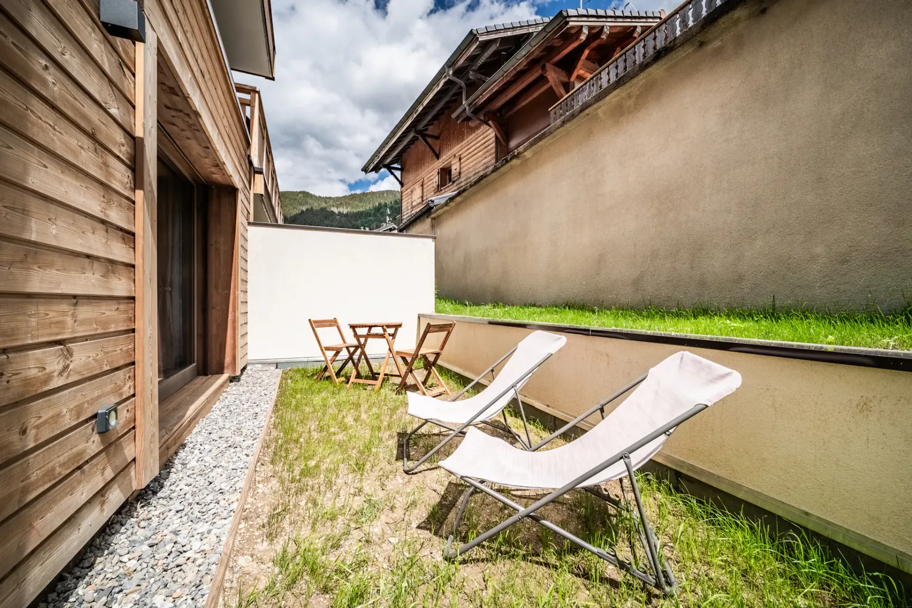Outdoor patio with lounge chairs, gravel path, and wooden-sided buildings.
