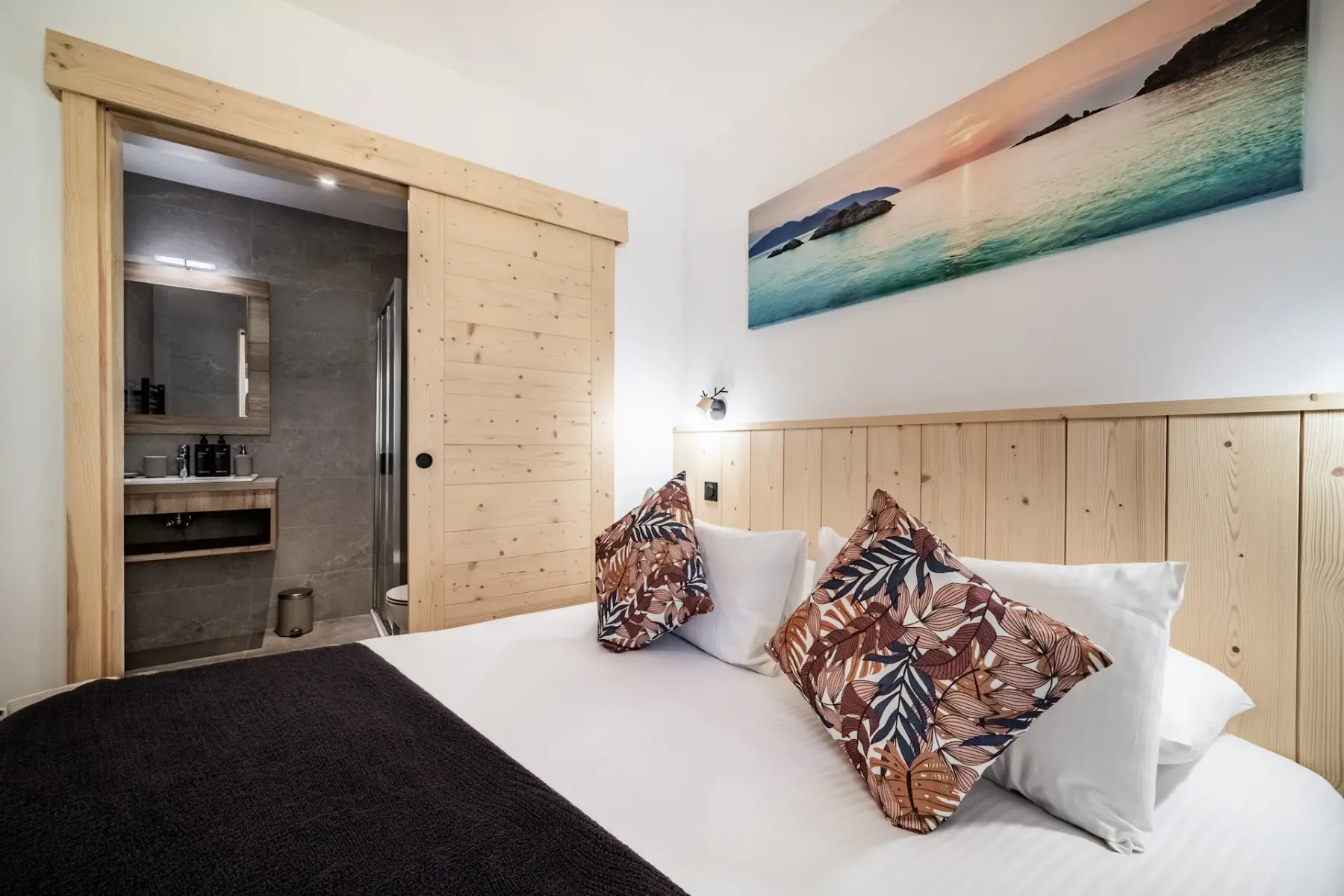 A bedroom with white bedding, patterned pillows, and a wooden headboard.