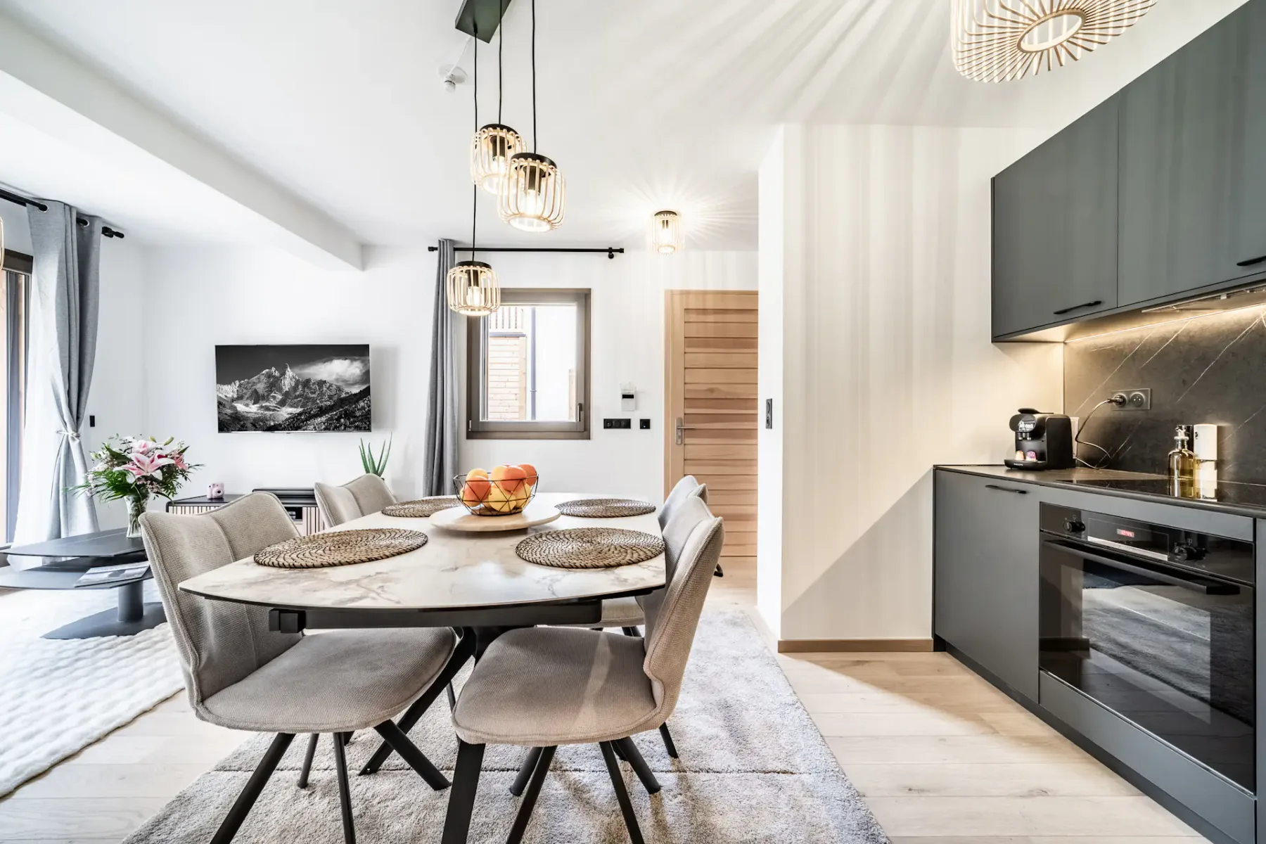 A bright dining area beside a modern kitchen, with a round table and pendant lights.
