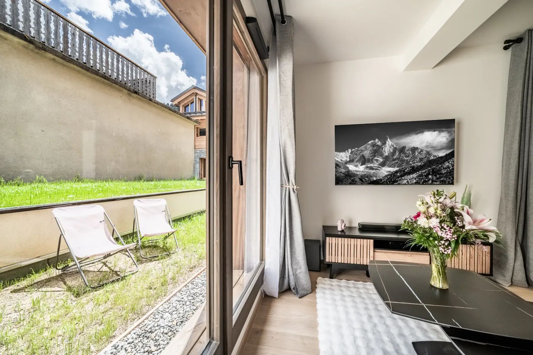A modern living room opens onto a small garden, with seating and a coffee table.