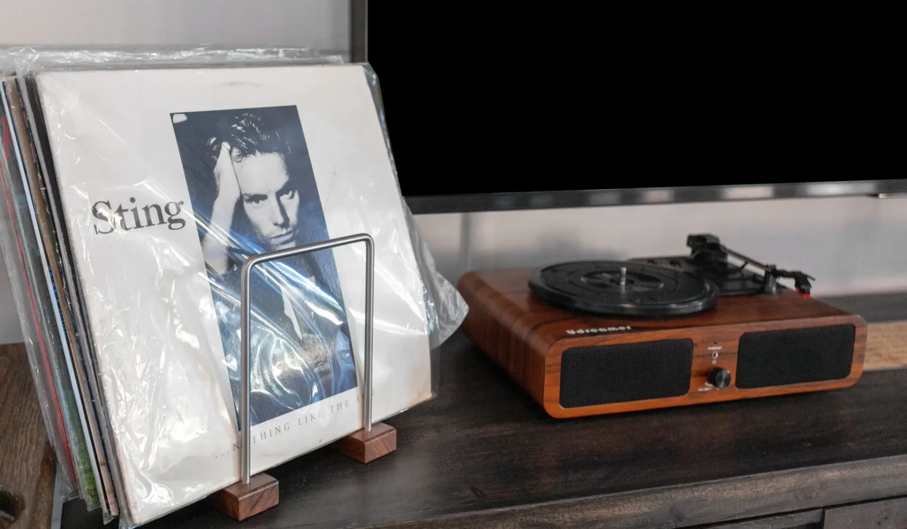 Un tocadiscos está junto a un disco de Sting expuesto sobre un estante oscuro.